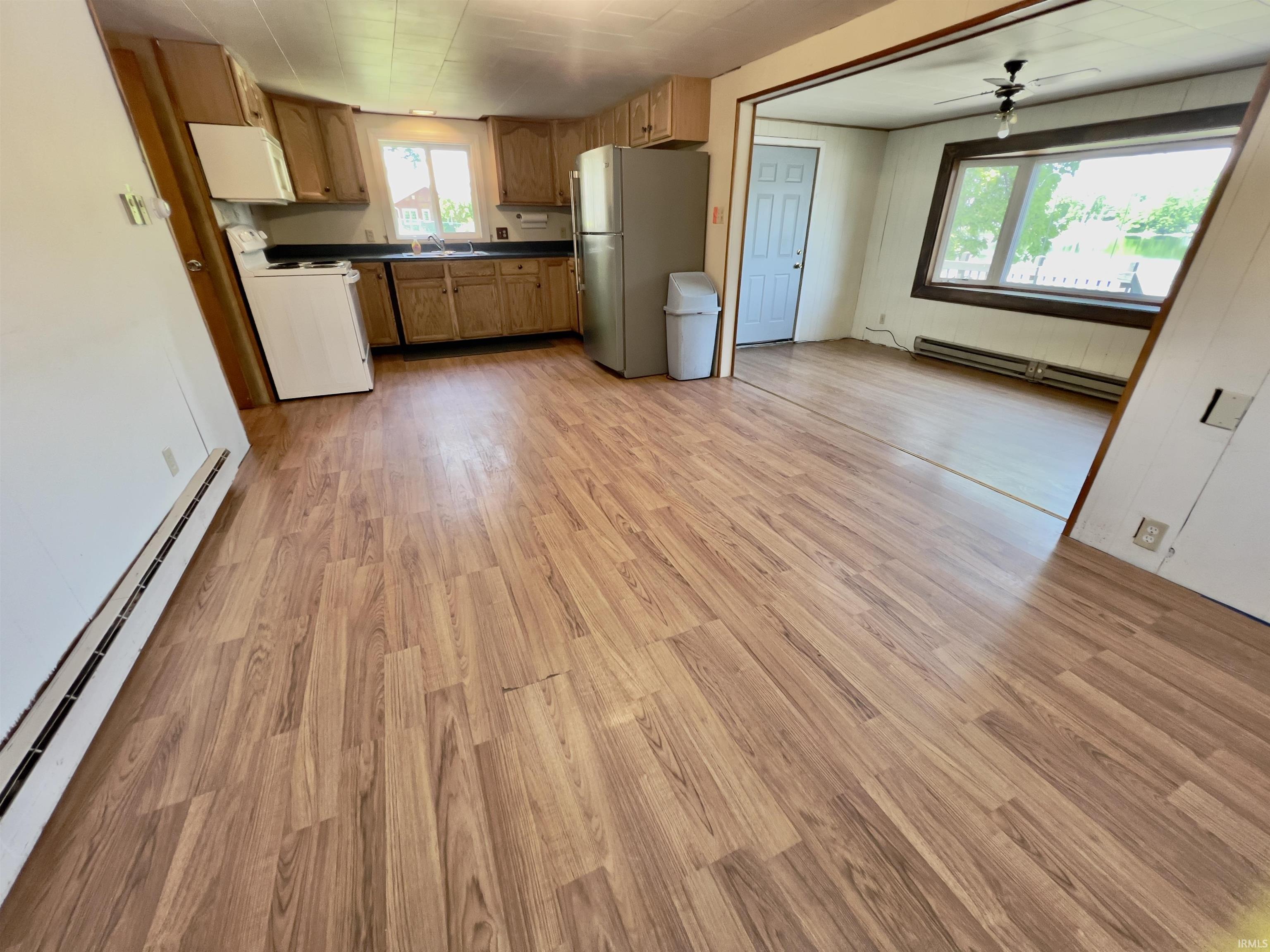 Kitchen and living area featuring wood-finish flooring, light wood cabinetry, white appliances, and a window overlooking exterior scenery