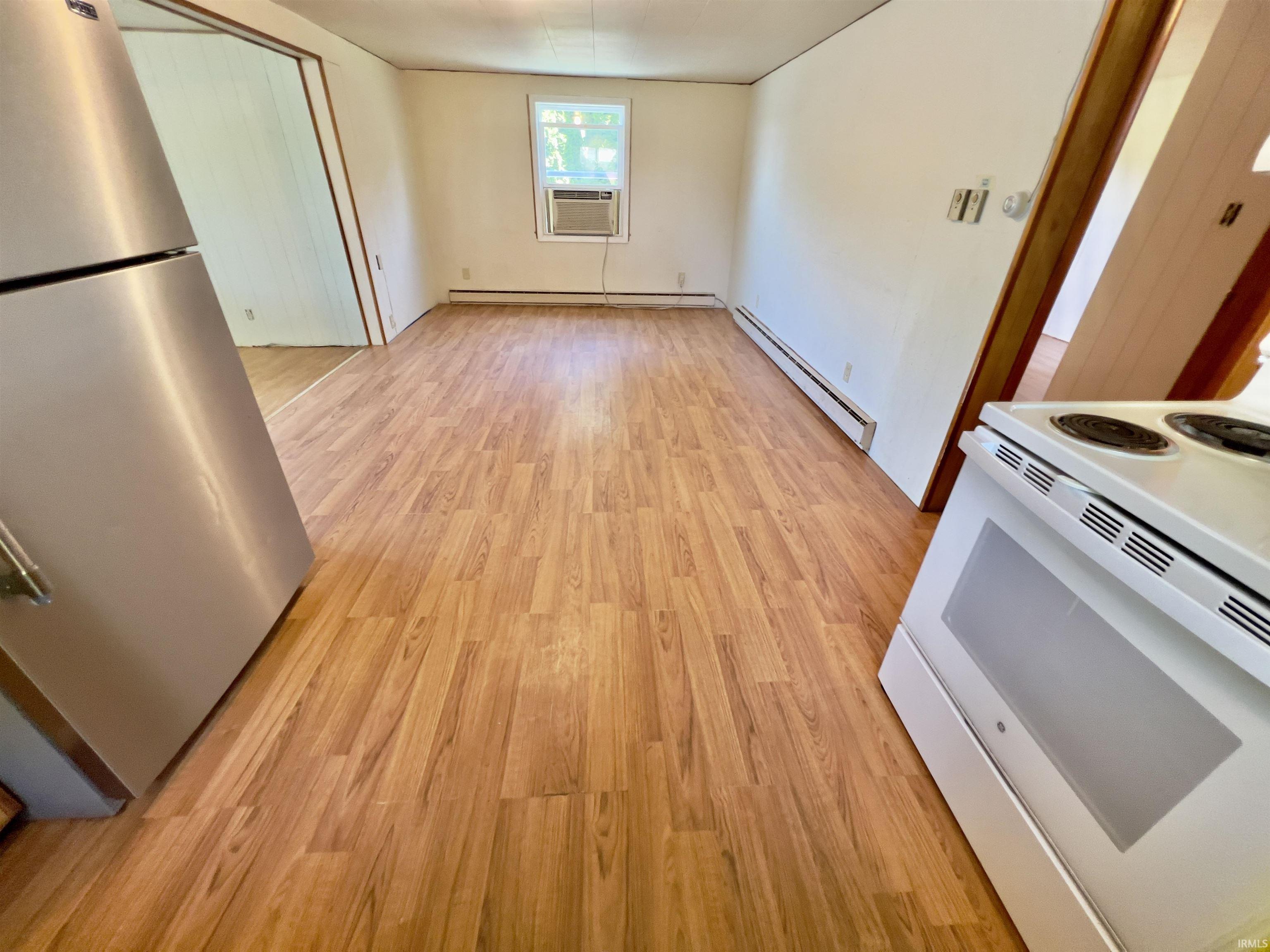 Open-concept dining area featuring wood-finish flooring, white walls, and a window with an installed air conditioning unit