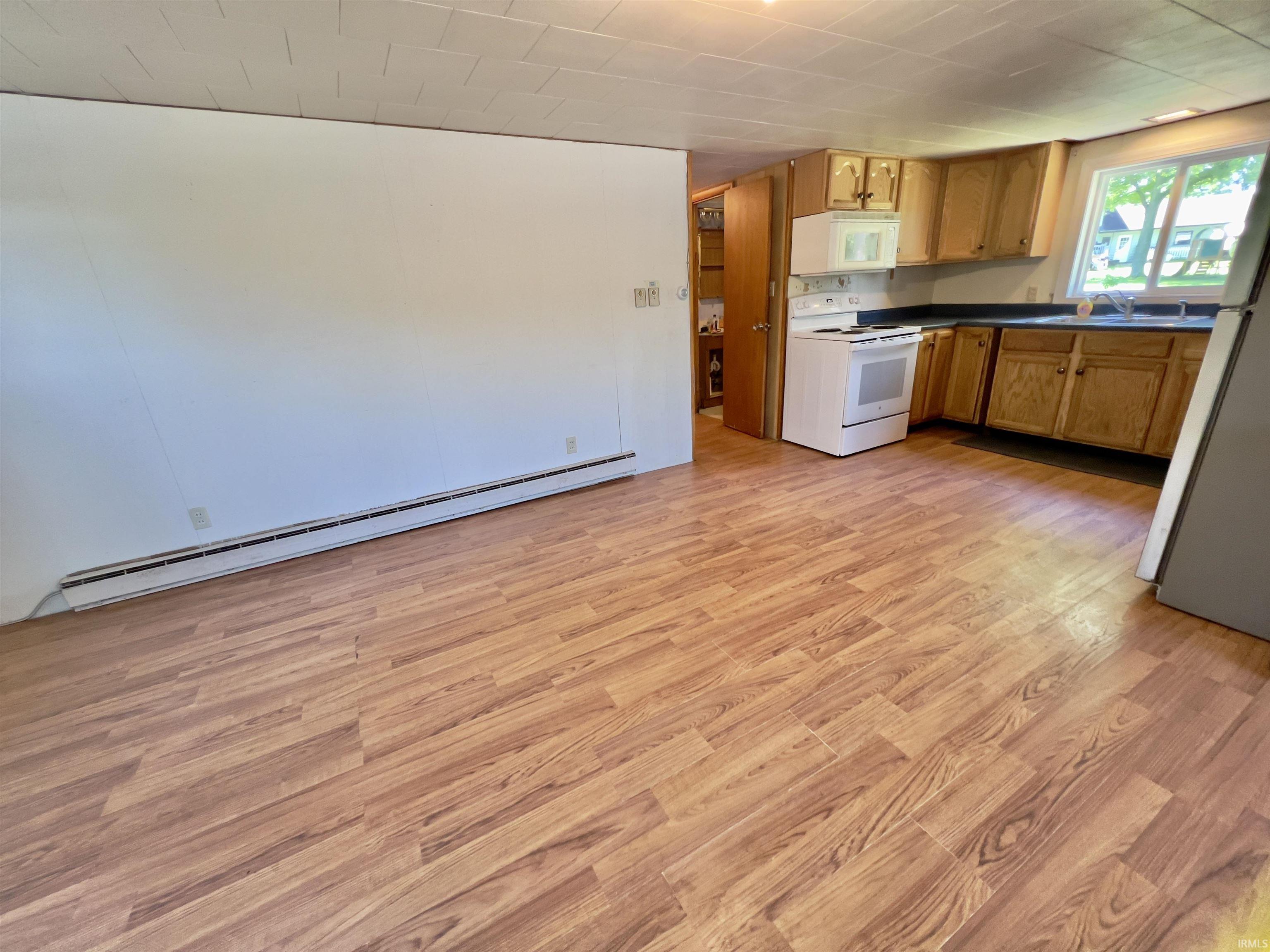 Kitchen space featuring wood-finish flooring, white appliances, dark countertops, and wood cabinetry
