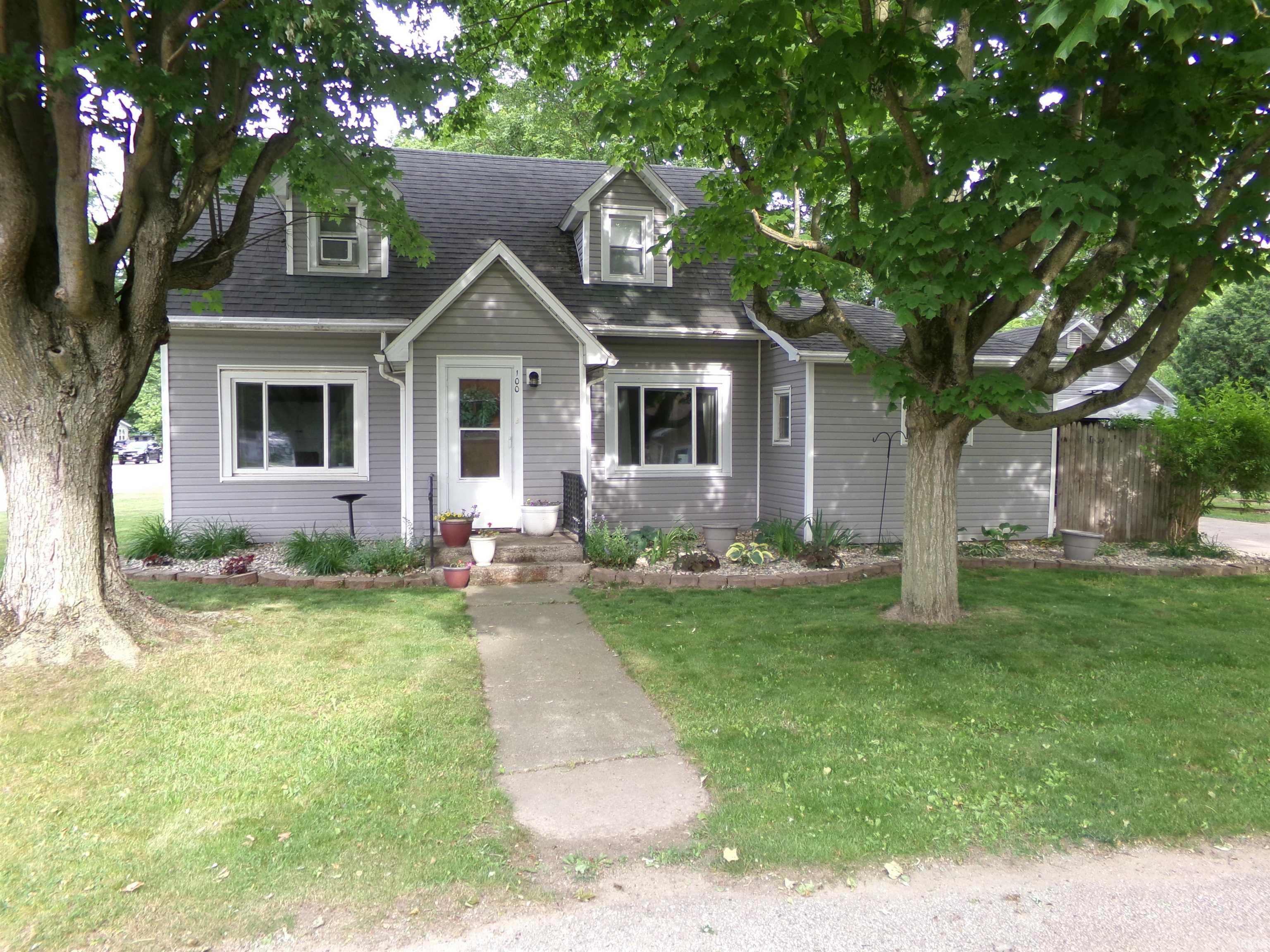 Charming dormer-style home featuring gray siding, a dark roof, and white-trimmed windows