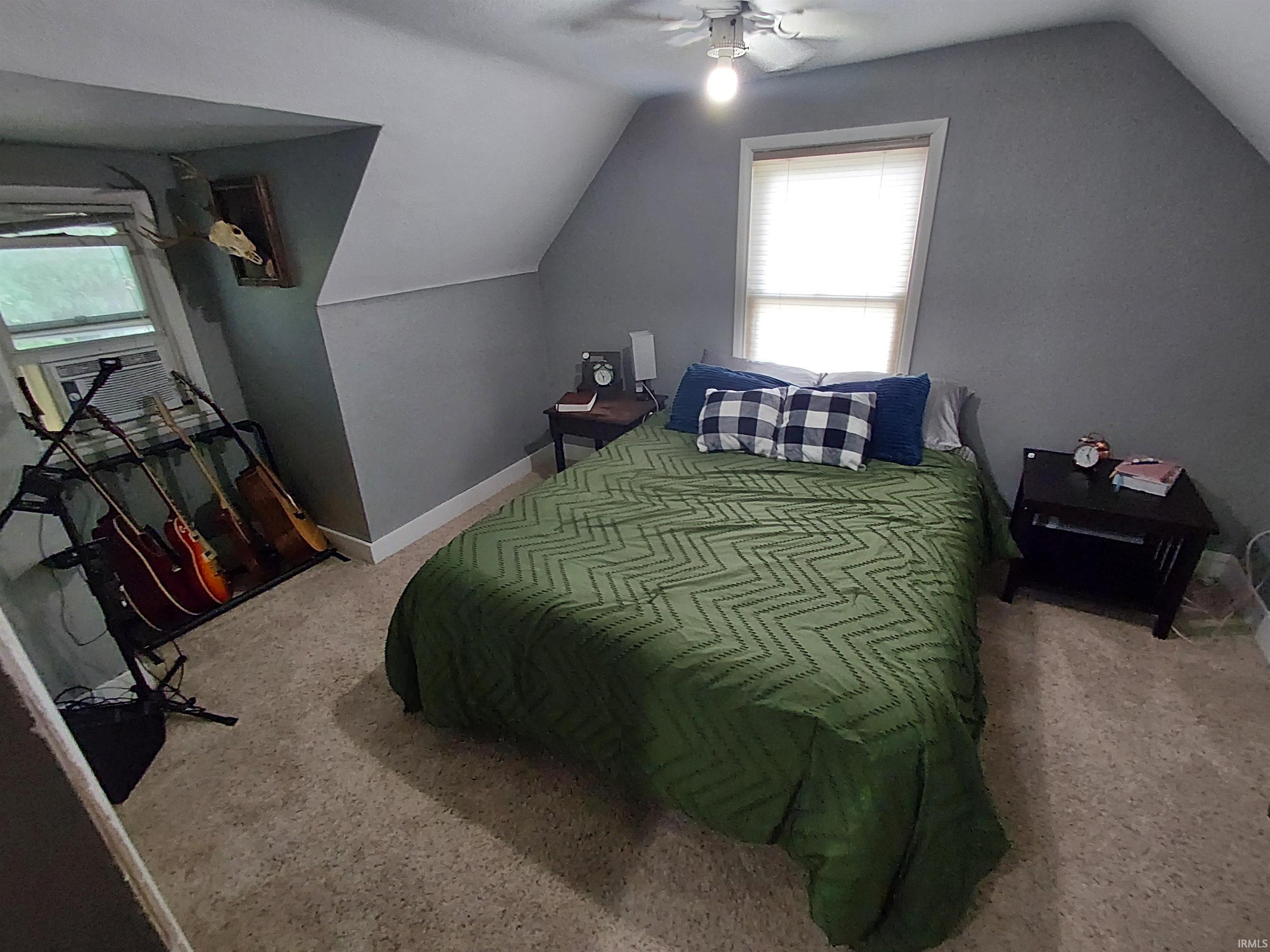 Attic bedroom featuring sloped ceilings, a window with horizontal blinds, and a built-in ceiling fan with lighting