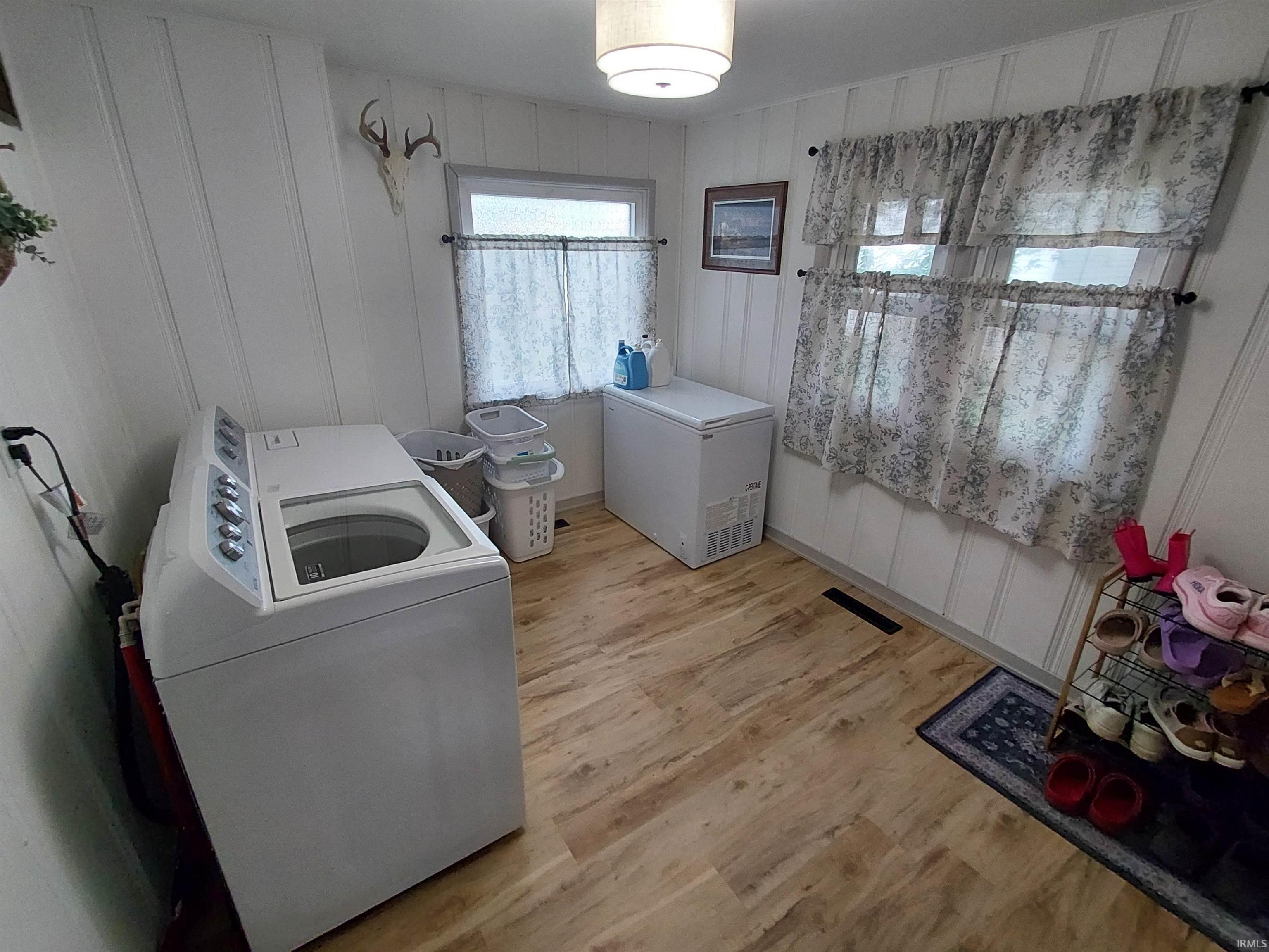 Laundry area featuring wood-finish flooring, white panel walls, and two windows