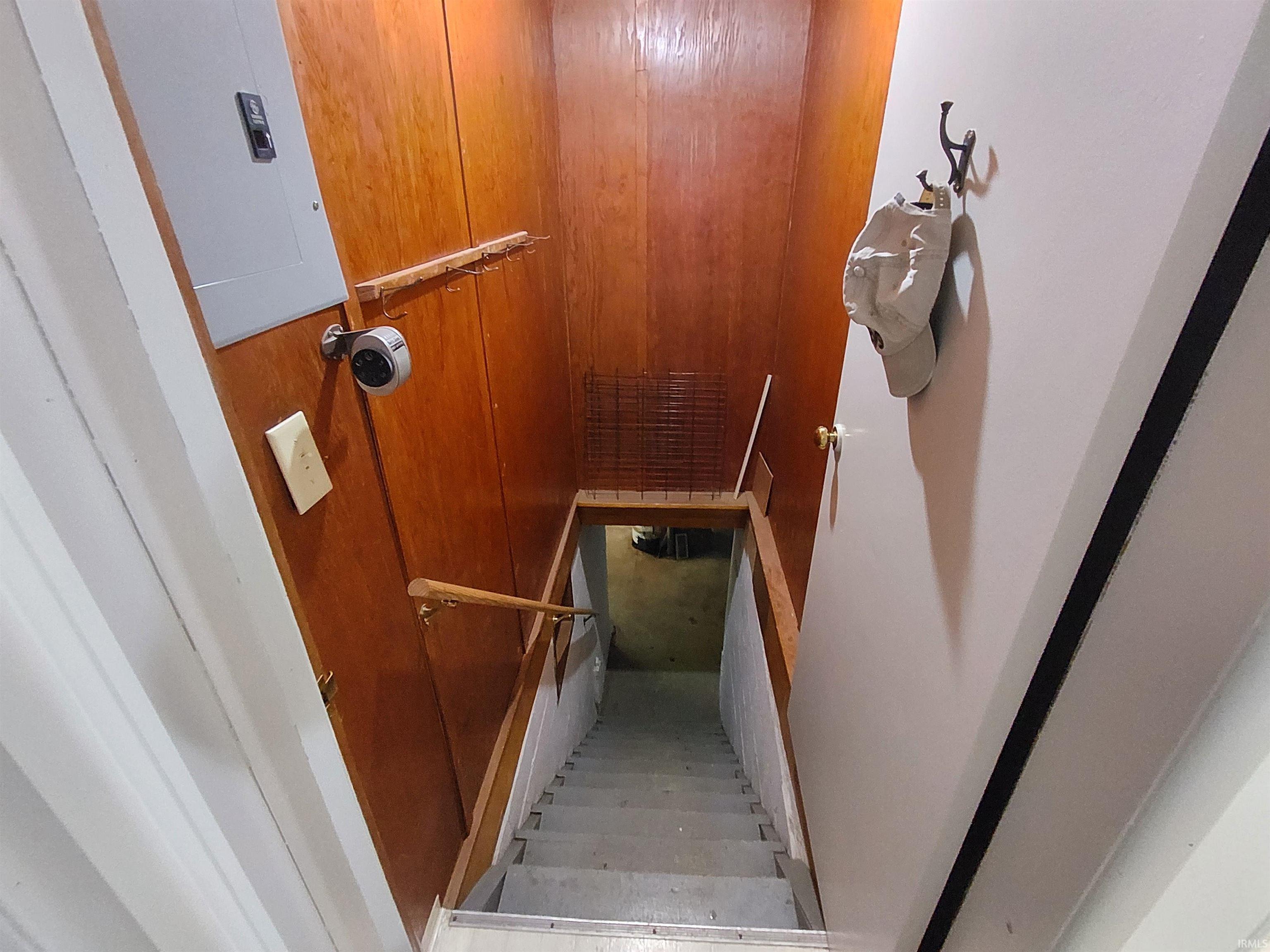 Stairwell with wood paneling, a white electrical panel, and a wooden handrail leading to a lower level