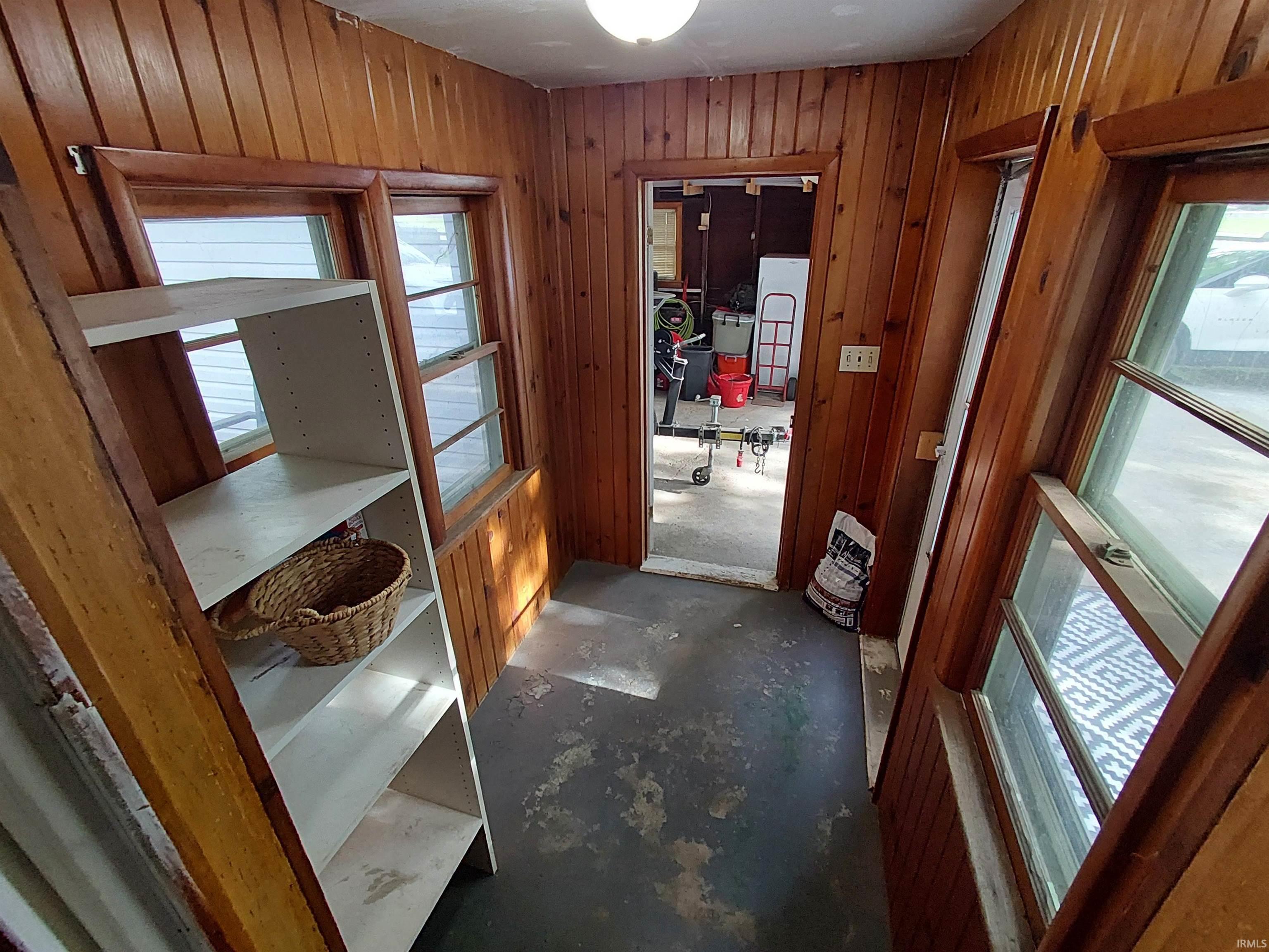 Enclosed entry space featuring wood-paneled walls, multiple windows, a ceiling-mounted light fixture, and a doorway opening to an additional area