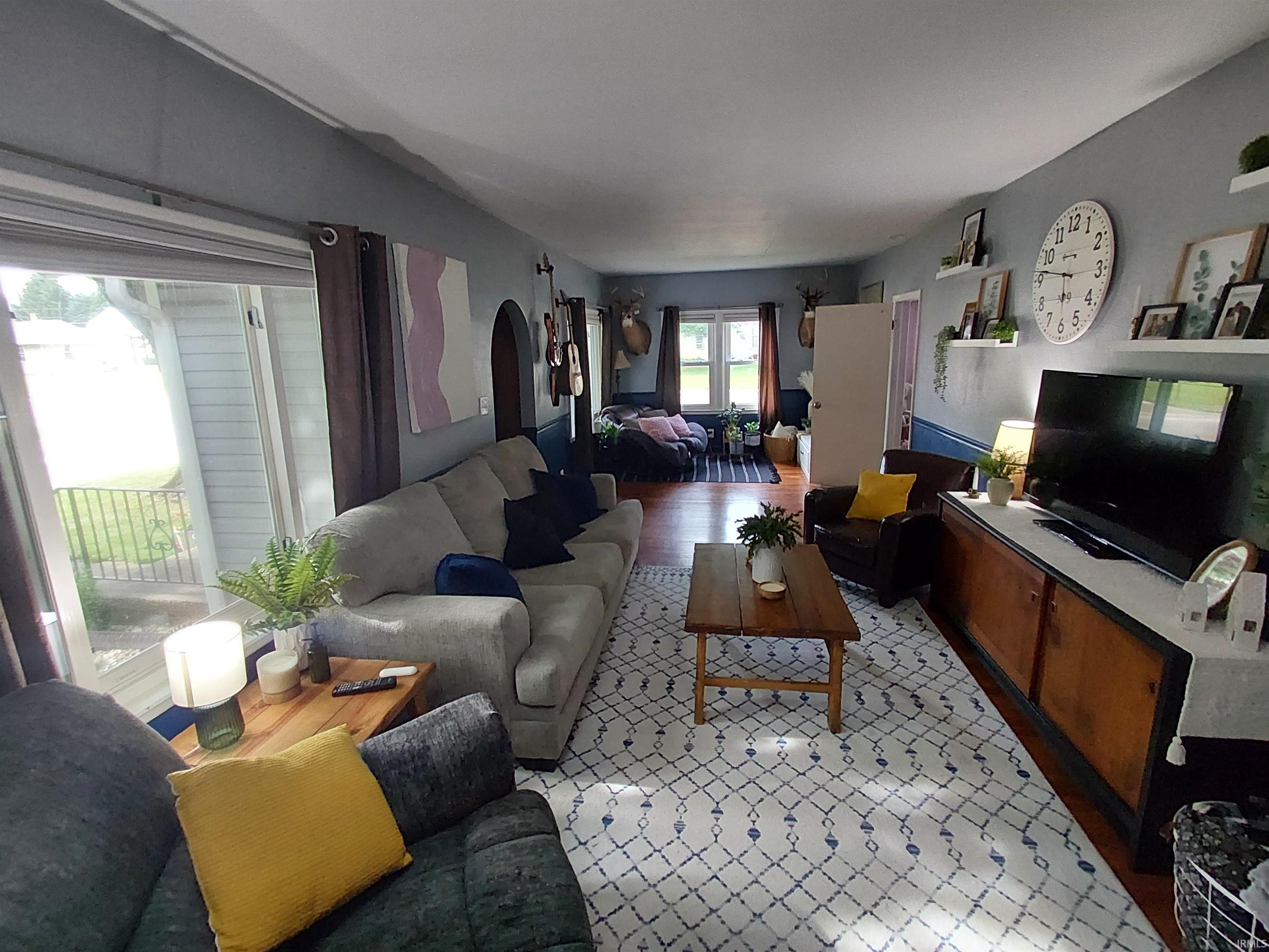 Spacious living area featuring large windows, wood-finish flooring, and a decorative arched doorway