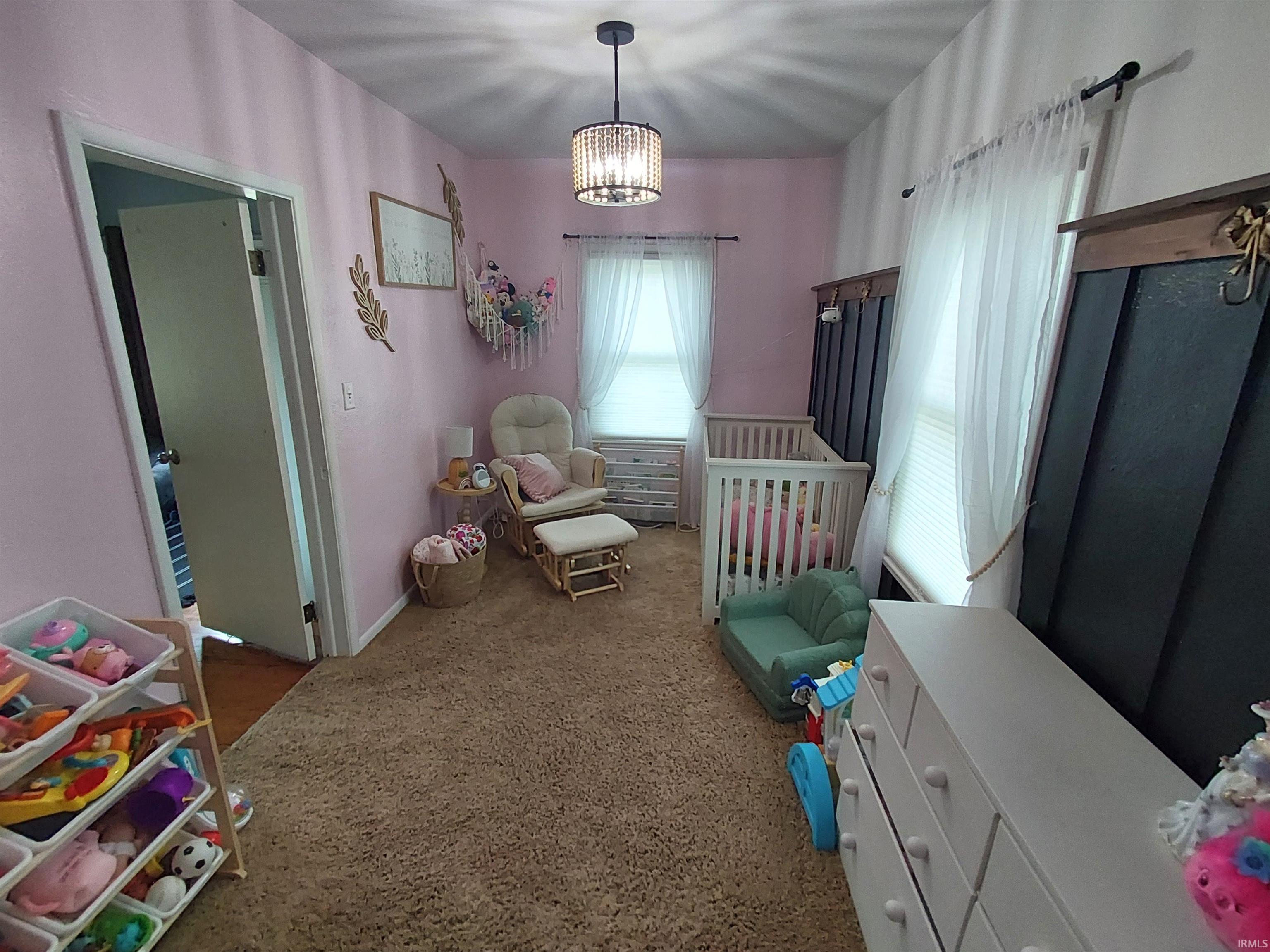 Carpeted room with a crystal-adorned ceiling light fixture, white trim, and two windows with white blinds and sheer curtains