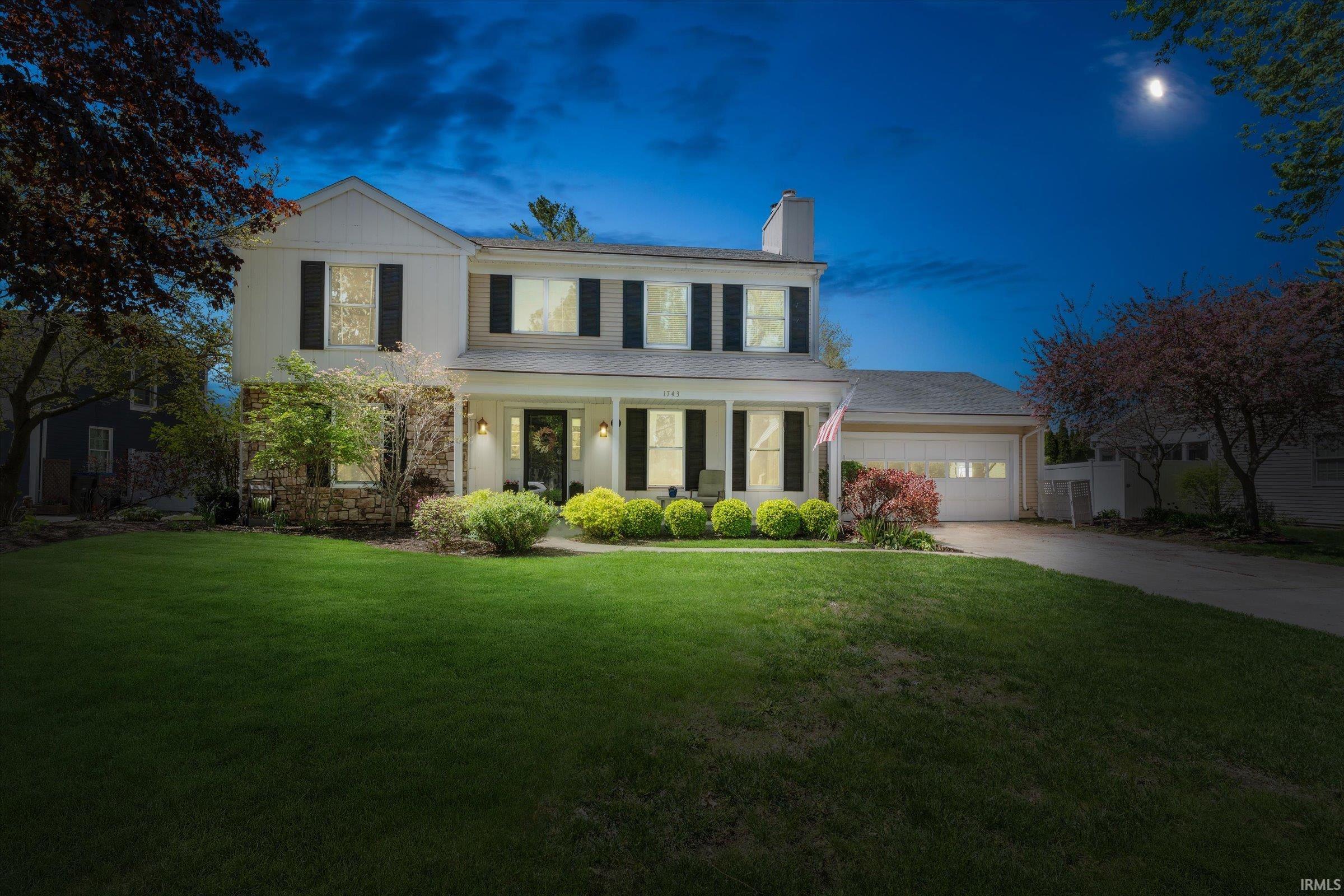 Two-story colonial residence featuring a white facade with dark shutters, a stone accent lower level, and a covered front porch with columns