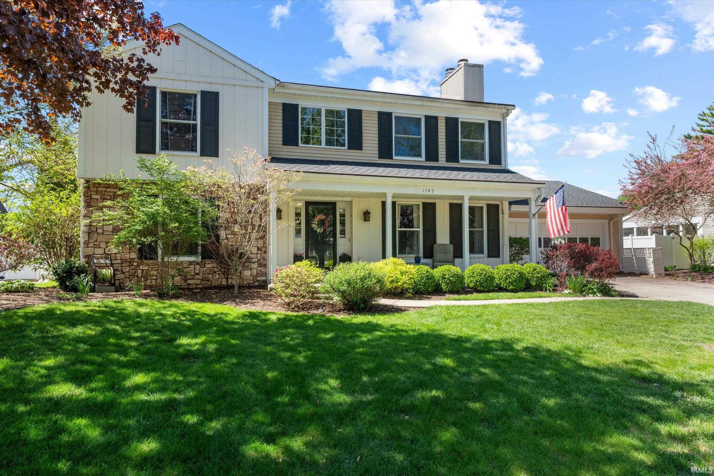 Traditional two-story residence with a stone and siding exterior, featuring a covered front porch with columns