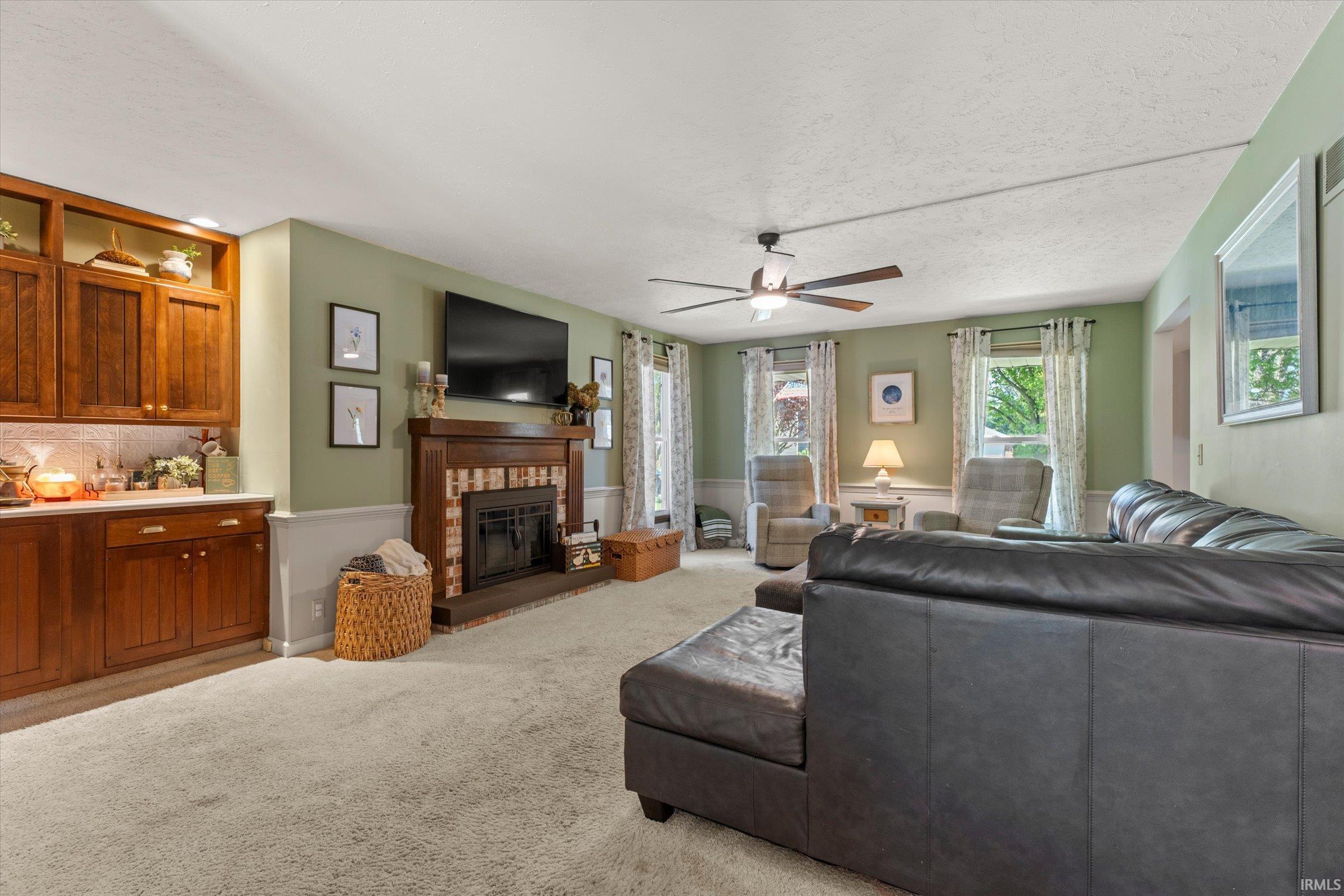 Living area featuring a brick fireplace with wood mantel, built-in cabinetry, ceiling fan, and carpet flooring
