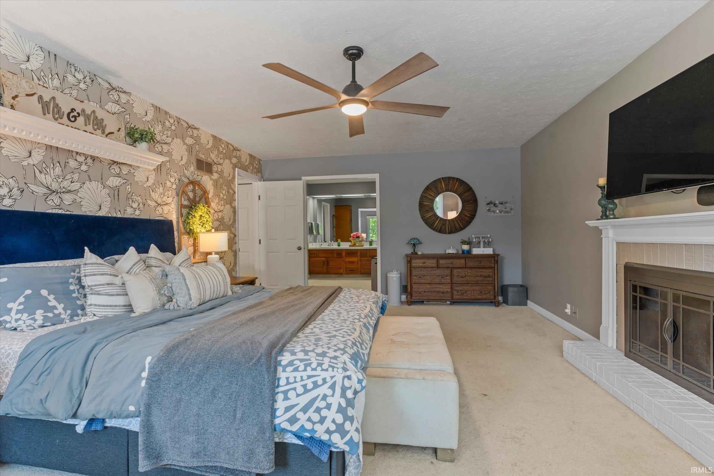 Interior room featuring a decorative accent wall with floral-patterned wallpaper, a ceiling fan with integrated lighting, and a fireplace with a white mantel and tile surround