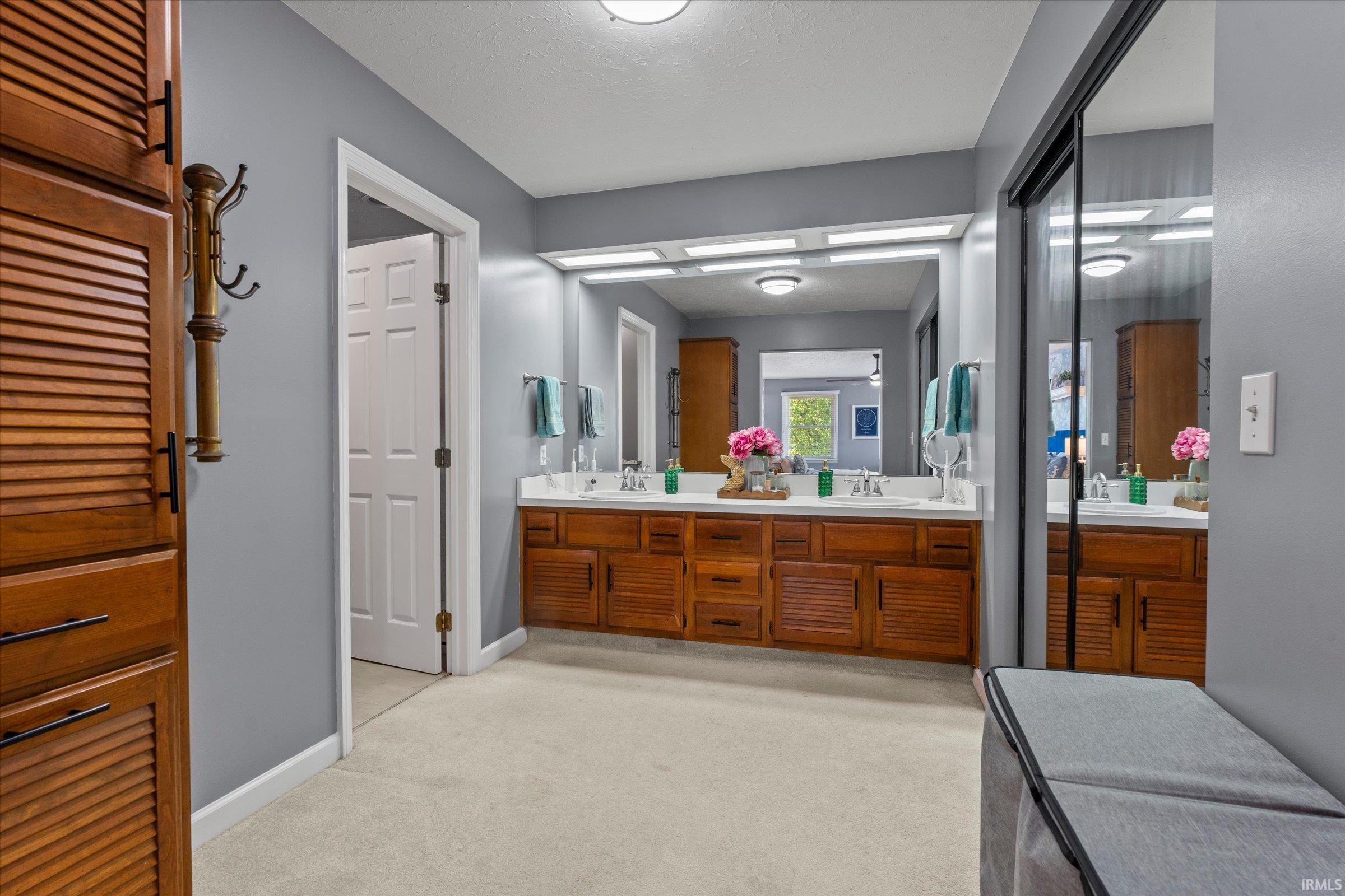 Double vanity featuring wood cabinetry with louvered doors, white countertops, and dual vessel sinks