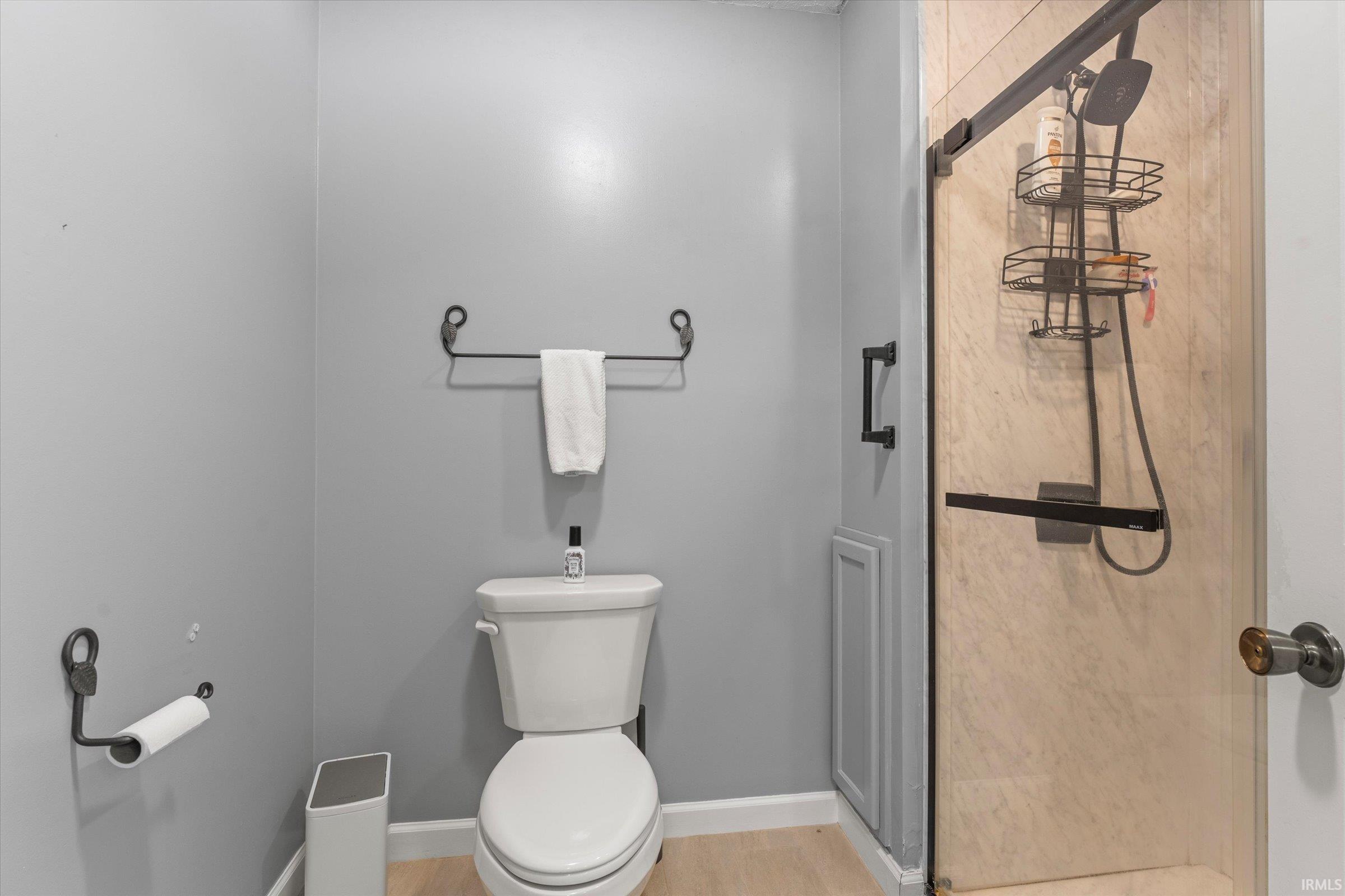 Bathroom featuring a glass-enclosed shower with a black-finish fixture, light wood-finish flooring, and a white toilet