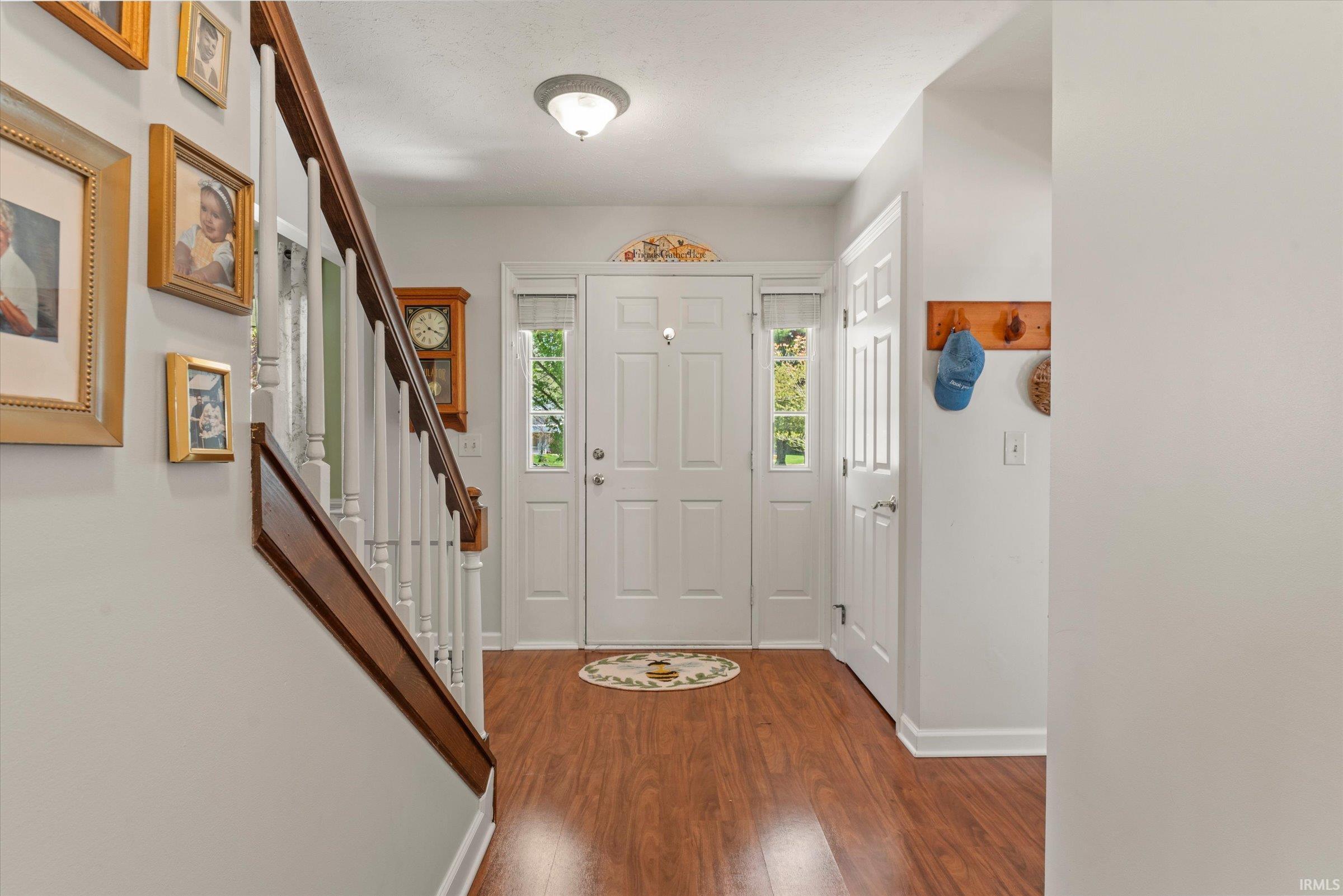 Entryway featuring wood-finish flooring, a white paneled front door with sidelights, and a staircase with stained wood handrails and white balusters