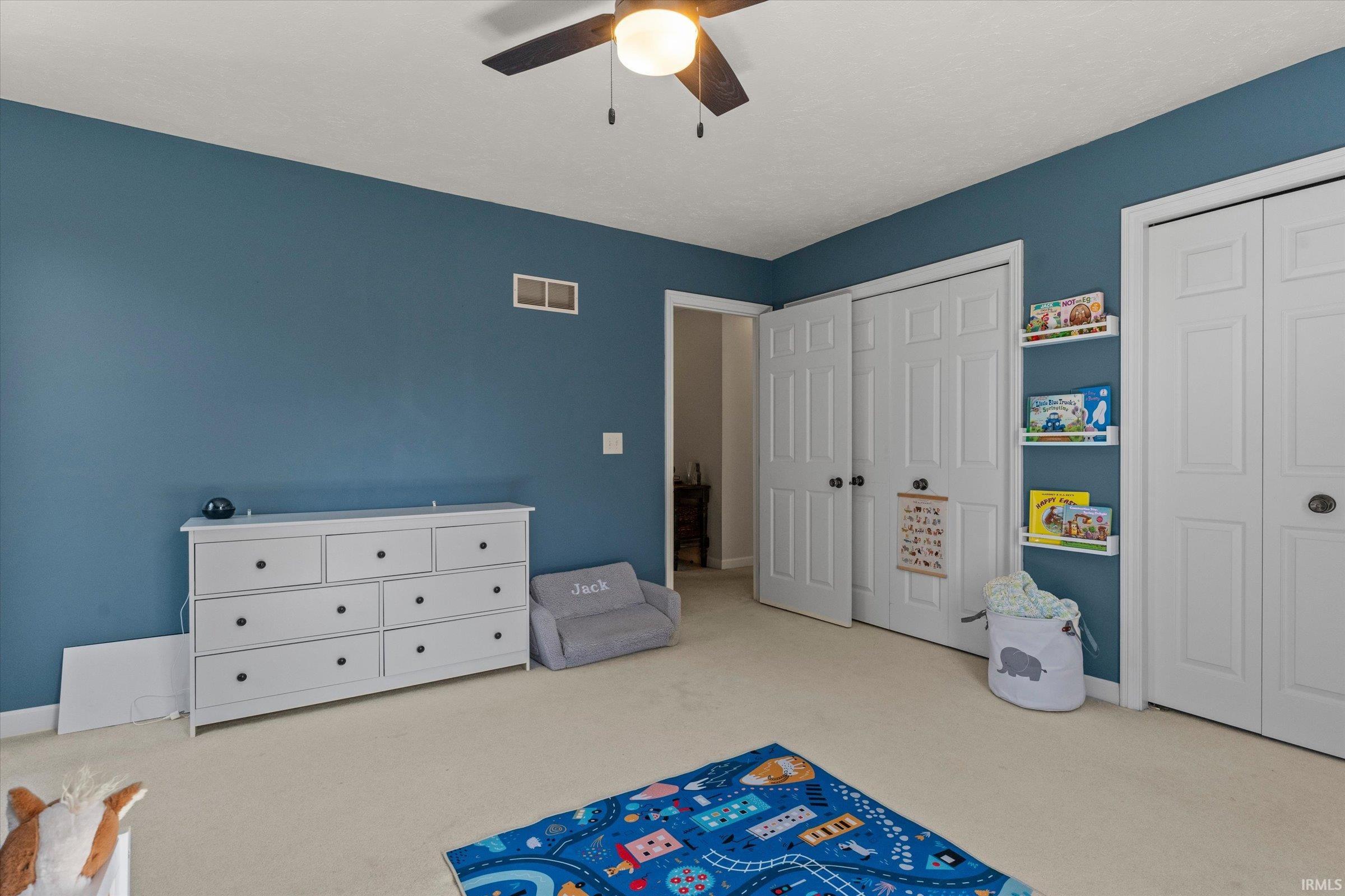 Room with blue walls, light-colored carpeting, a ceiling fan with integrated lighting, and white bi-fold closet doors