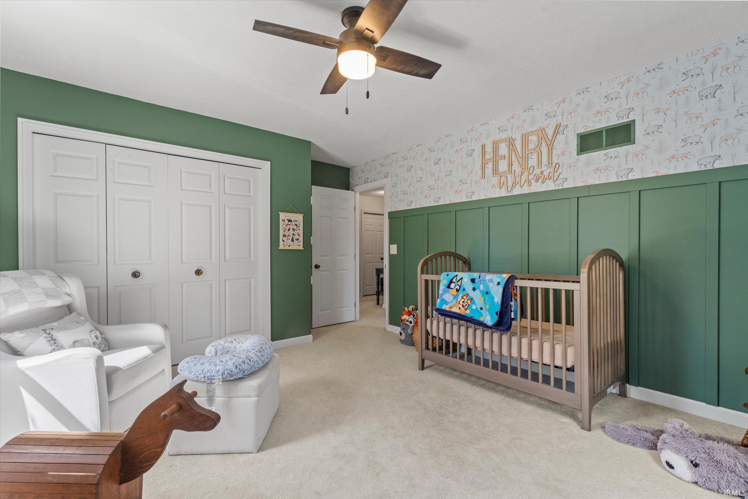 Carpeted room featuring a ceiling fan with integrated lighting, bi-fold closet doors, a green accent wall, and board and batten paneling