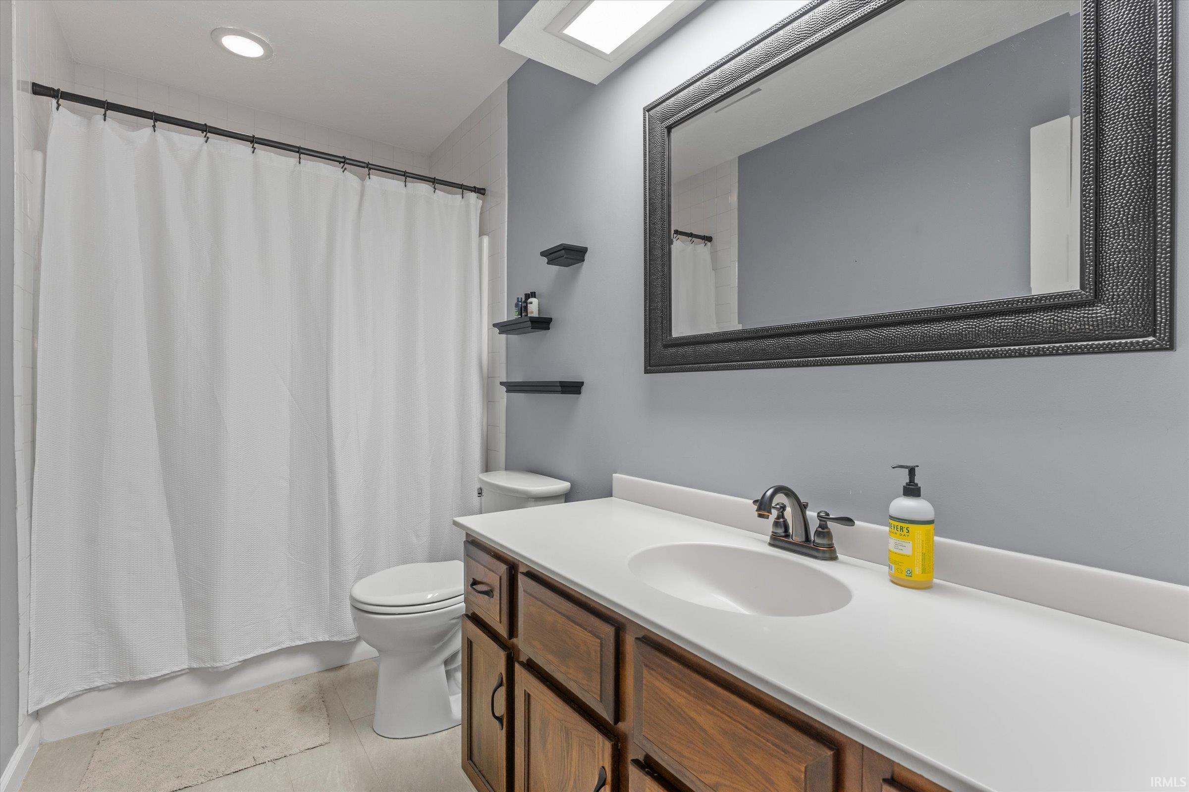 Bathroom featuring a wood-finish vanity with a white countertop, an undermount sink, and a framed mirror