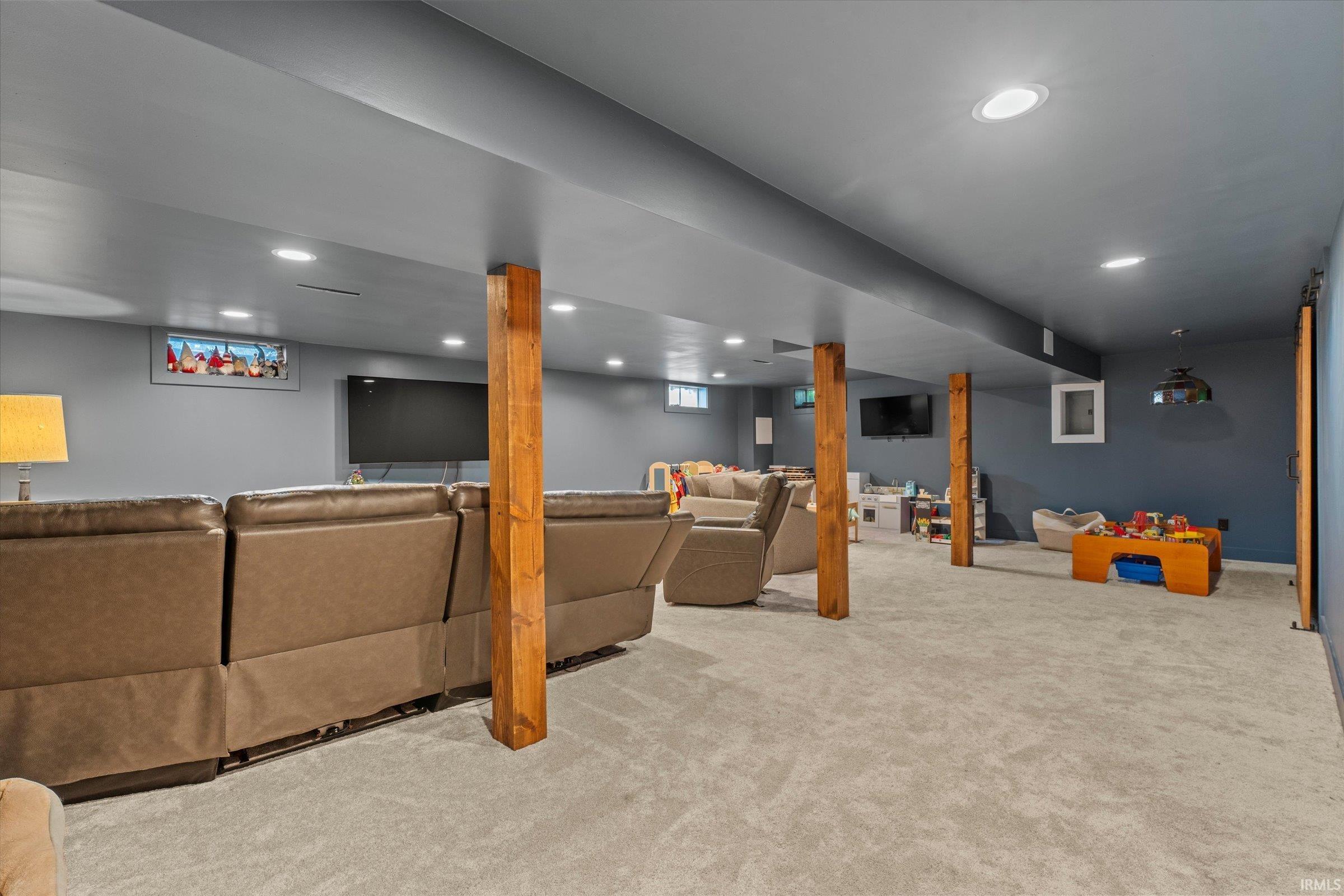 Spacious lower level featuring recessed lighting, light gray carpeting, exposed wood support beams, and a window with a decorative insert