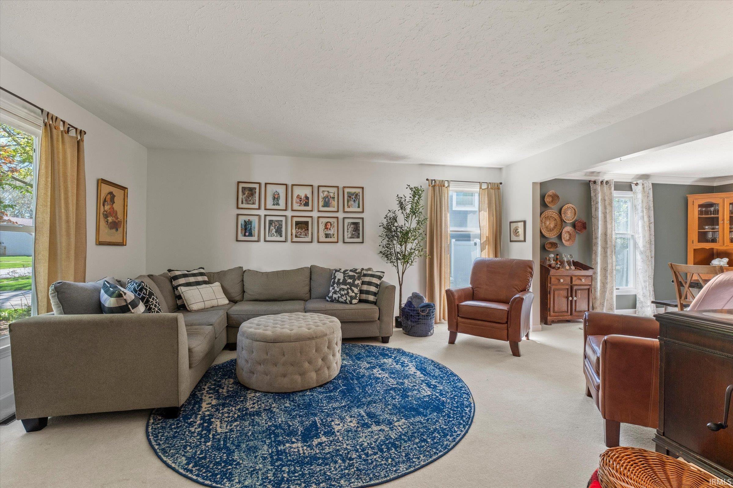 Expansive living area featuring light-colored carpeting, multiple windows with natural light, and a dedicated dining space visible beyond a wide entryway