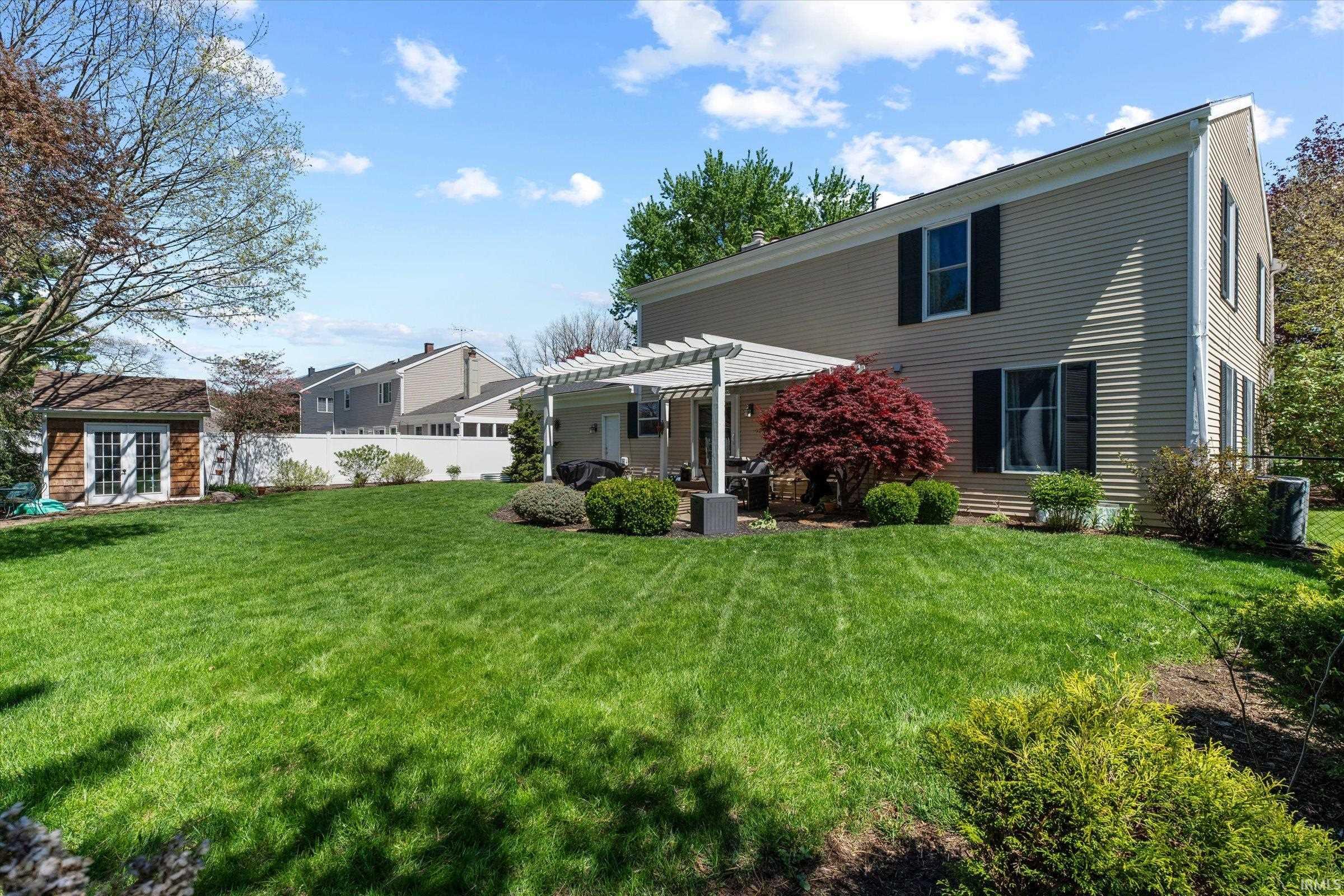 Expansive lawn area featuring a pergola-covered patio, mature red-leafed tree, and a detached shed with double doors