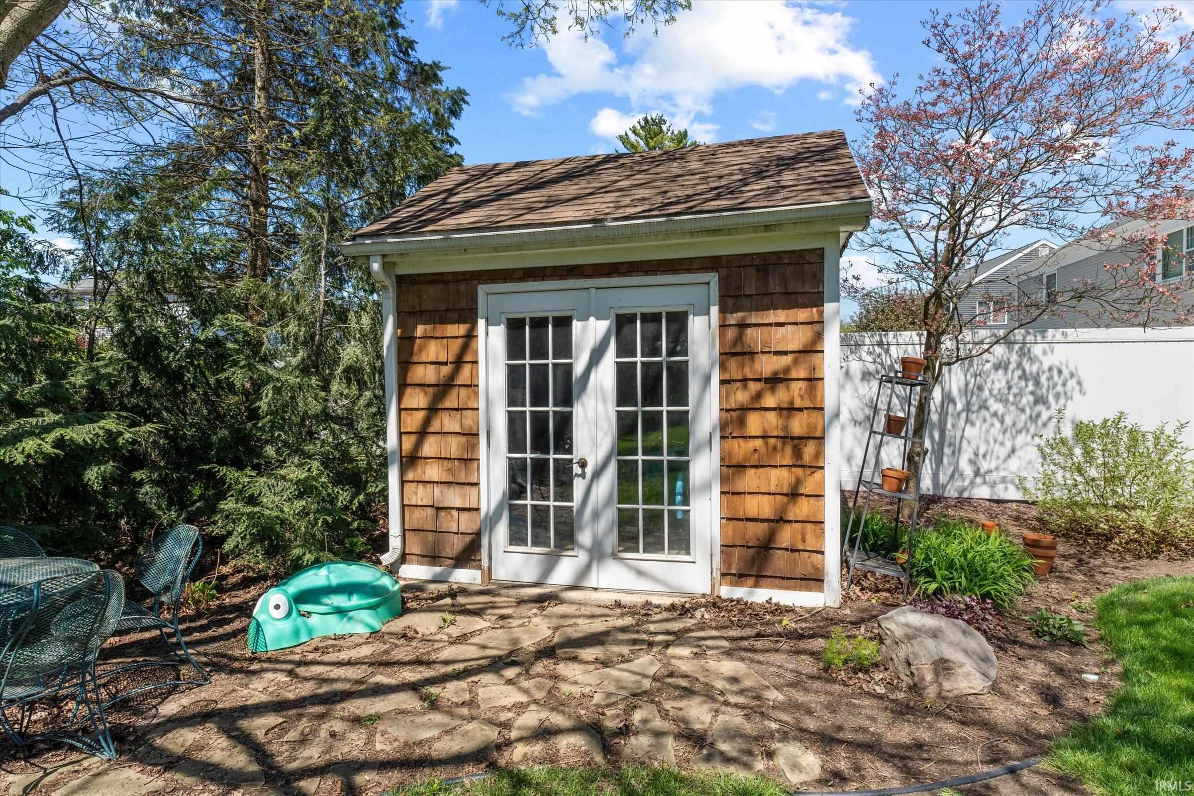 Shingled outbuilding featuring double French doors, a natural stone patio, and mature landscaping