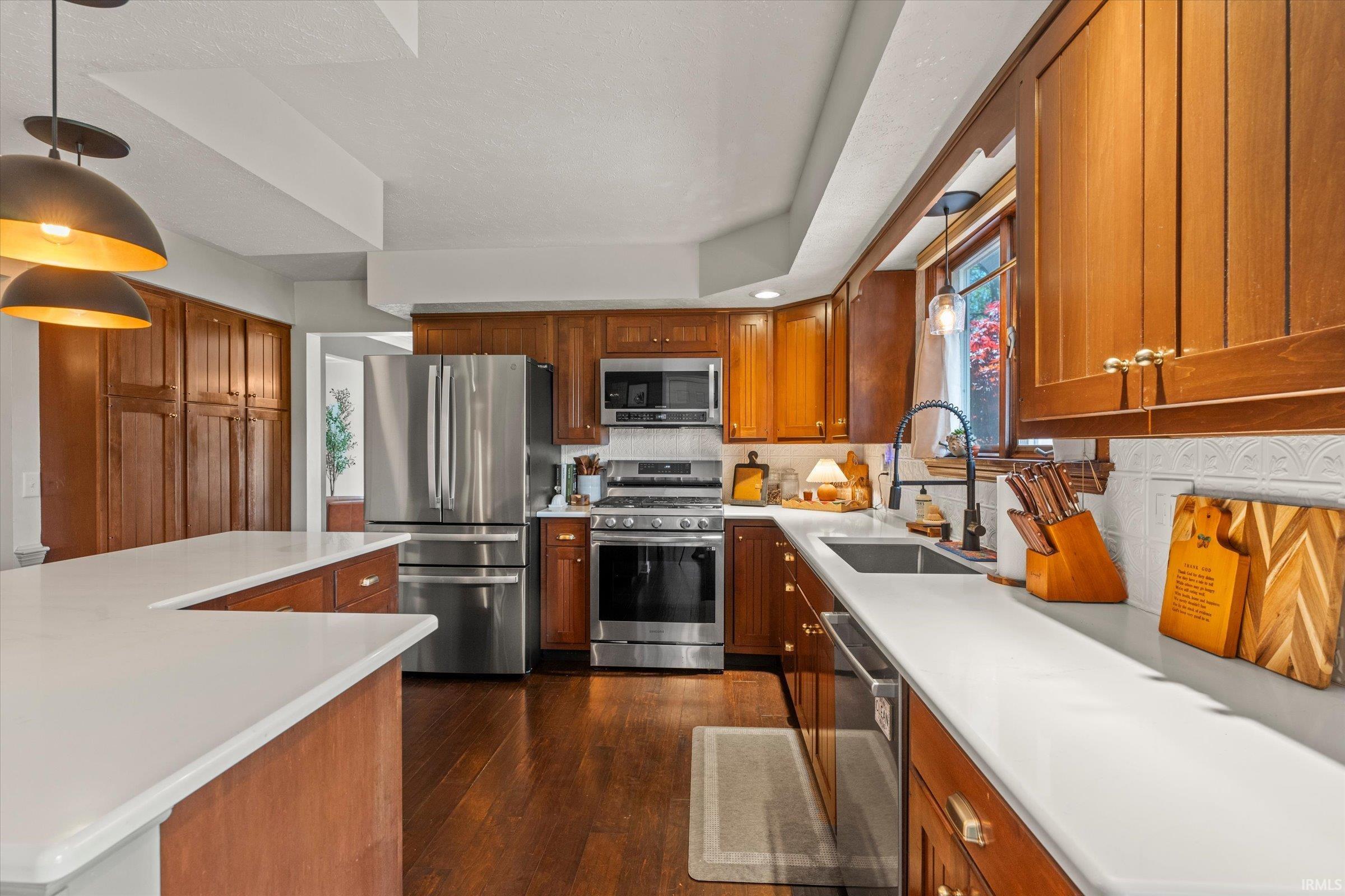 Kitchen featuring wood-finish cabinetry, stainless steel appliances, white countertops, and wood-finish flooring