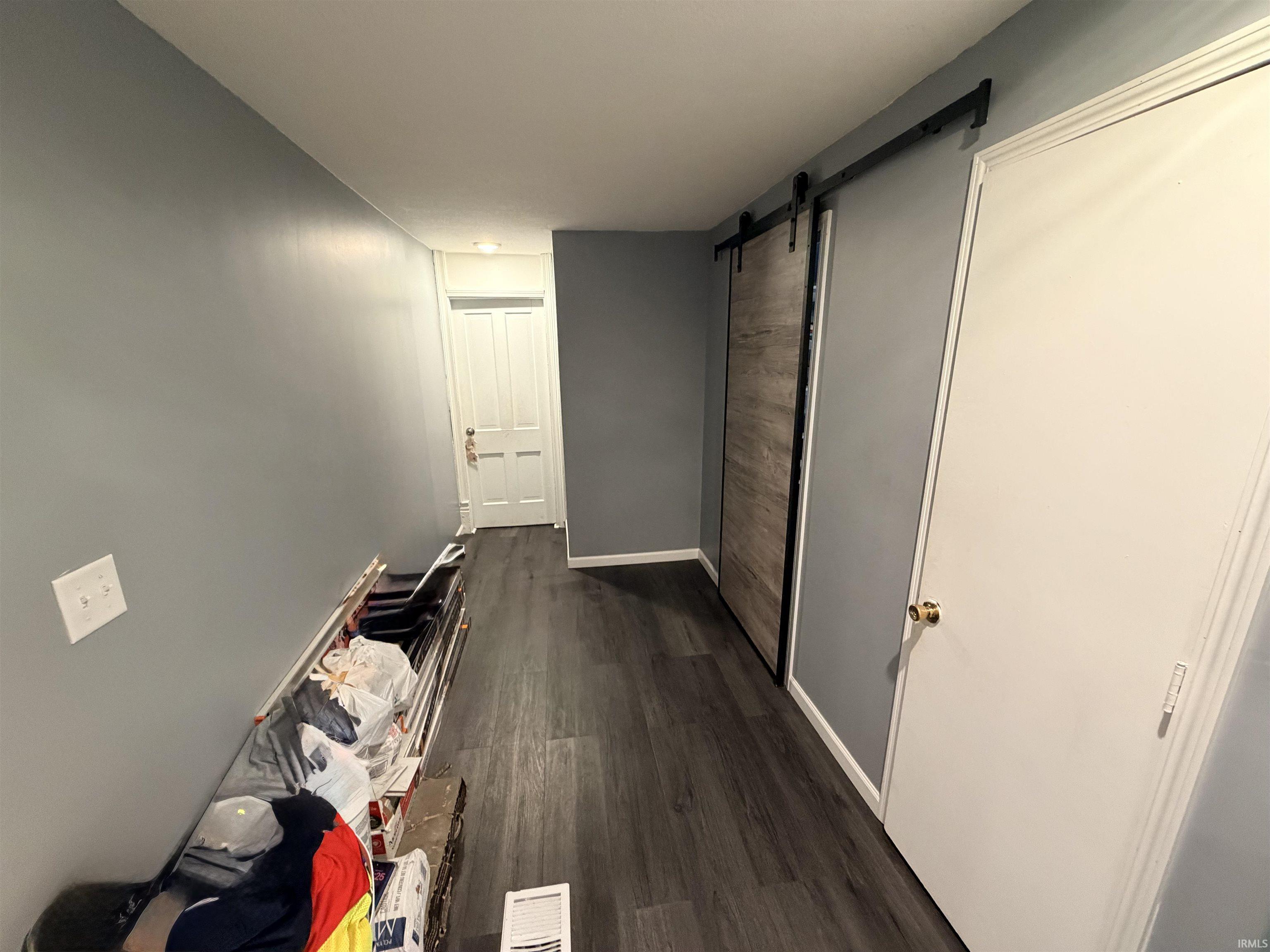 Hallway featuring wood-finish flooring, a barn door with black hardware, and gray painted walls