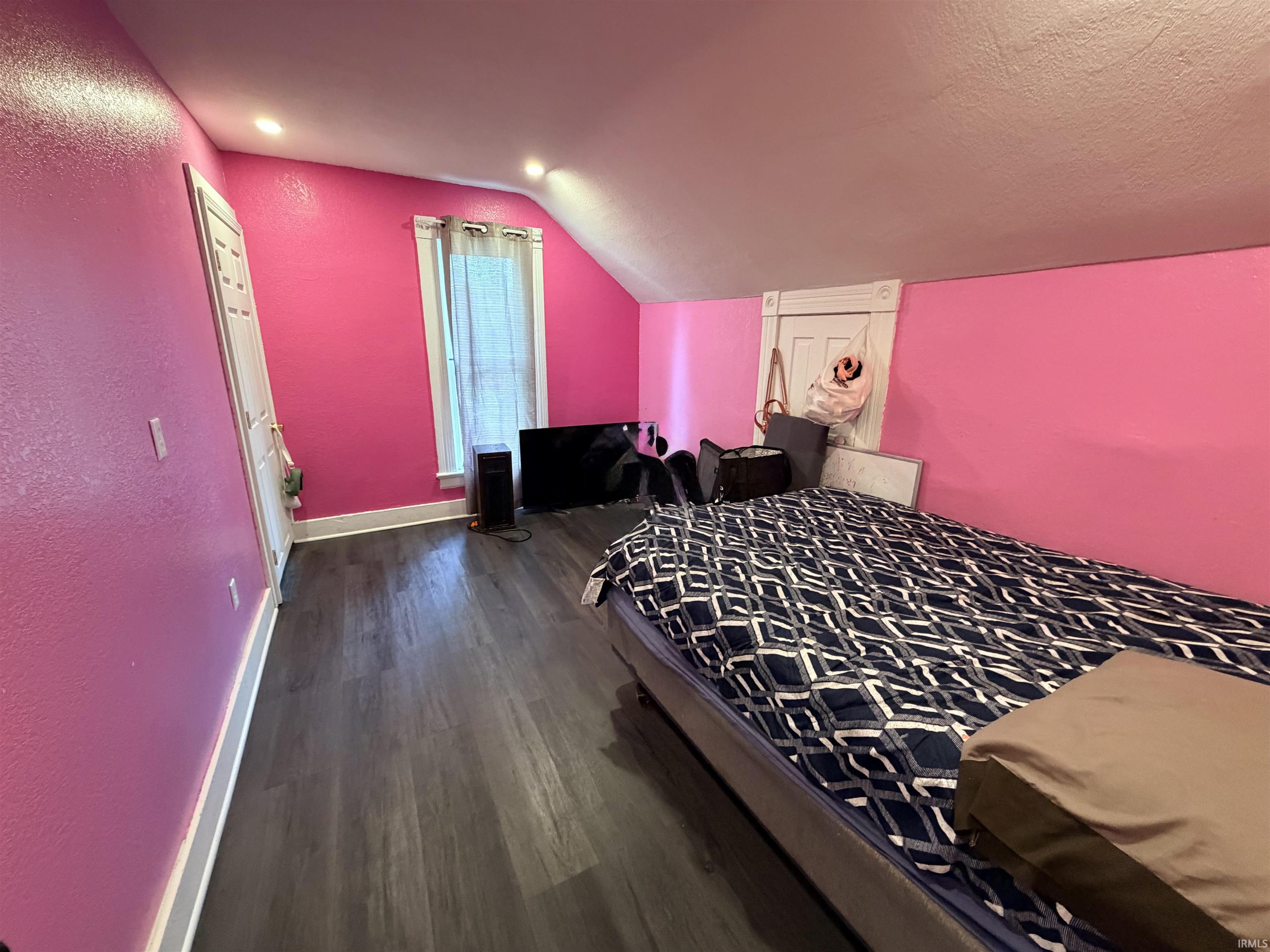 Attic space featuring wood-finish flooring and a window with white trim
