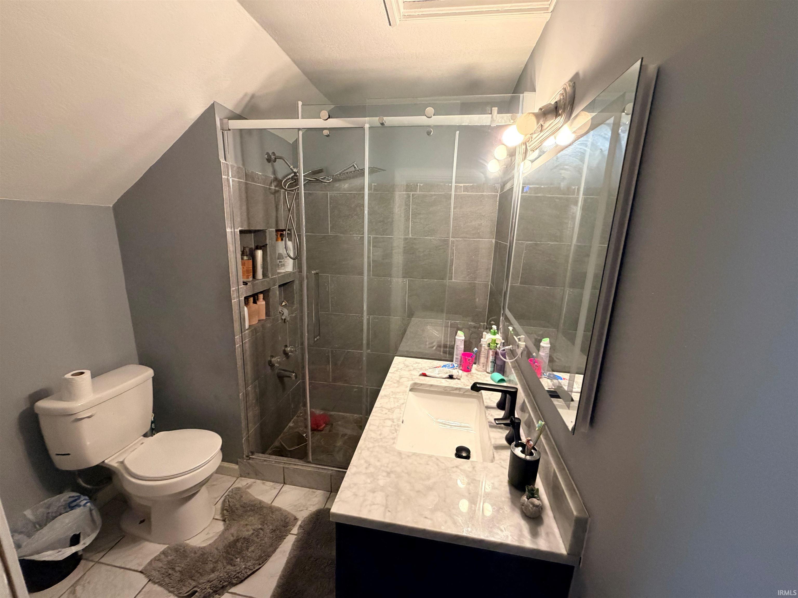 Contemporary bathroom featuring a spacious shower with dark gray tile surround and integrated shelving, a sliding glass enclosure, and modern fixtures