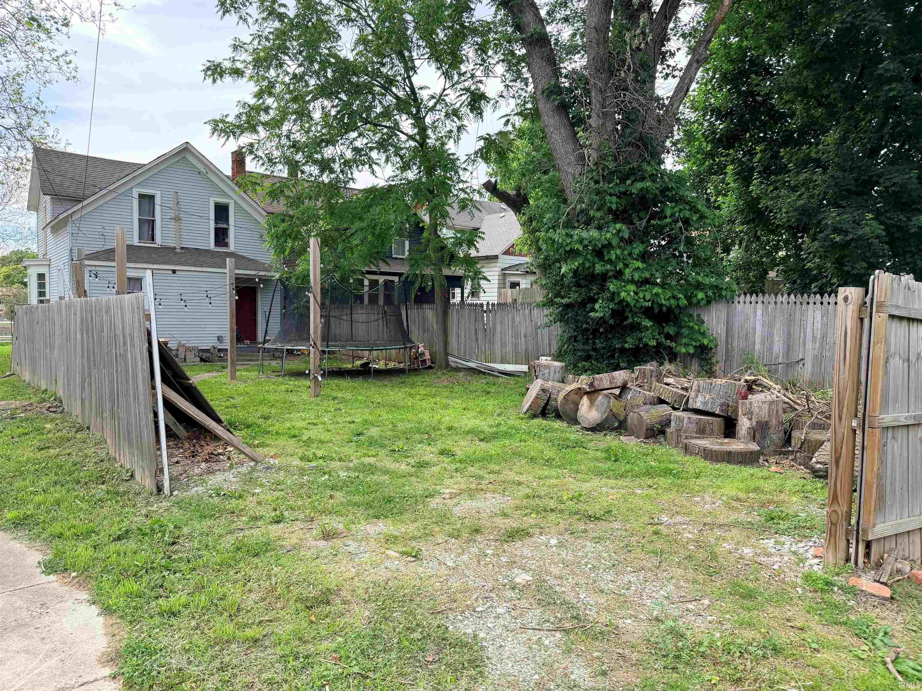 Fenced backyard with mature trees and a substantial wood pile