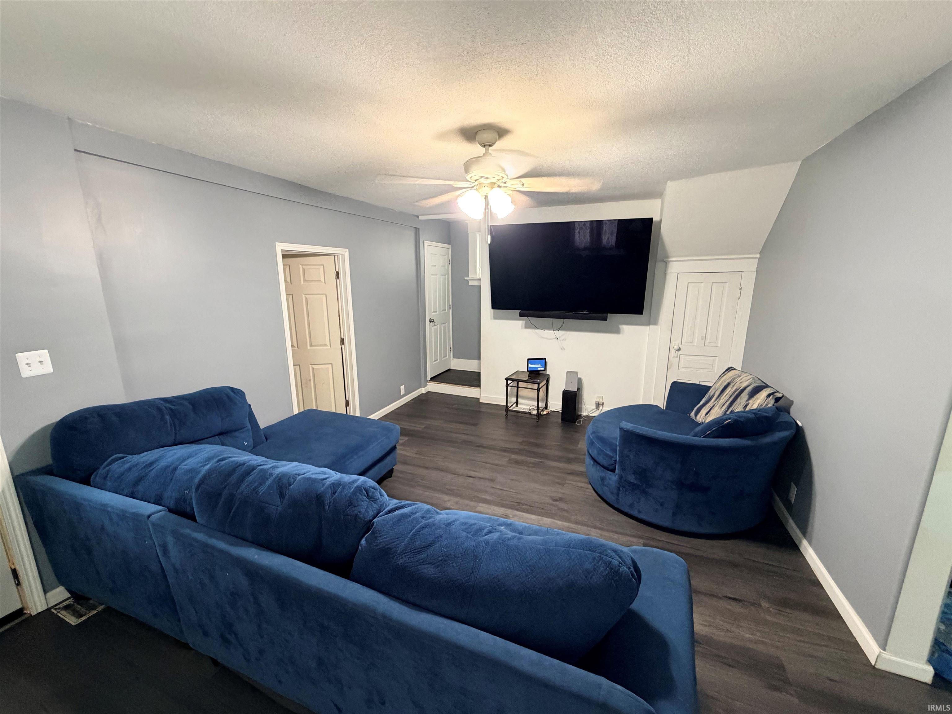 Spacious living area featuring dark wood-finish flooring, light grey painted walls, and white baseboards