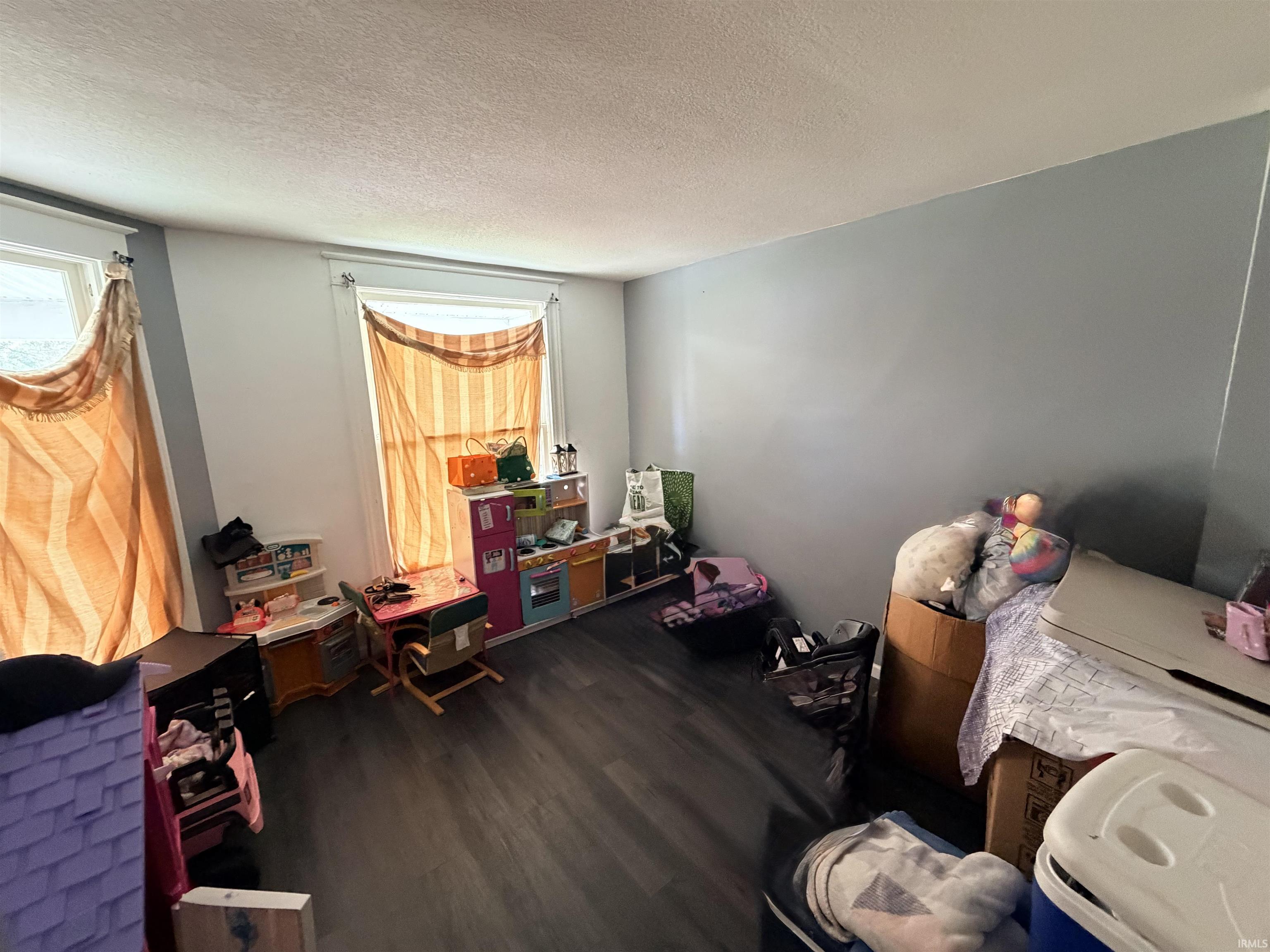 Spacious room featuring two windows with natural light, wood-finish flooring, and light blue walls