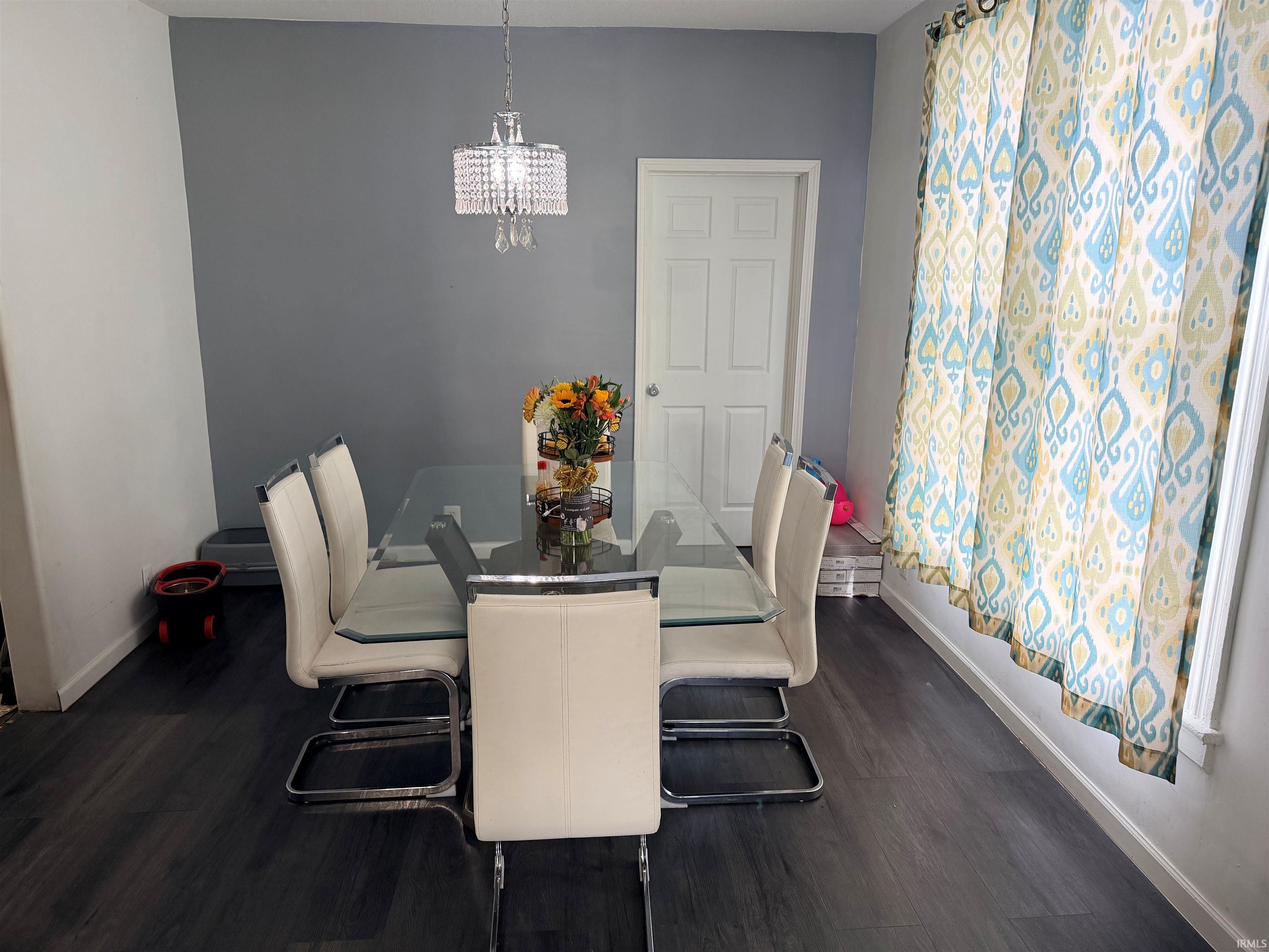 Dining area featuring dark wood-finish flooring, a contemporary chandelier, and a white paneled door