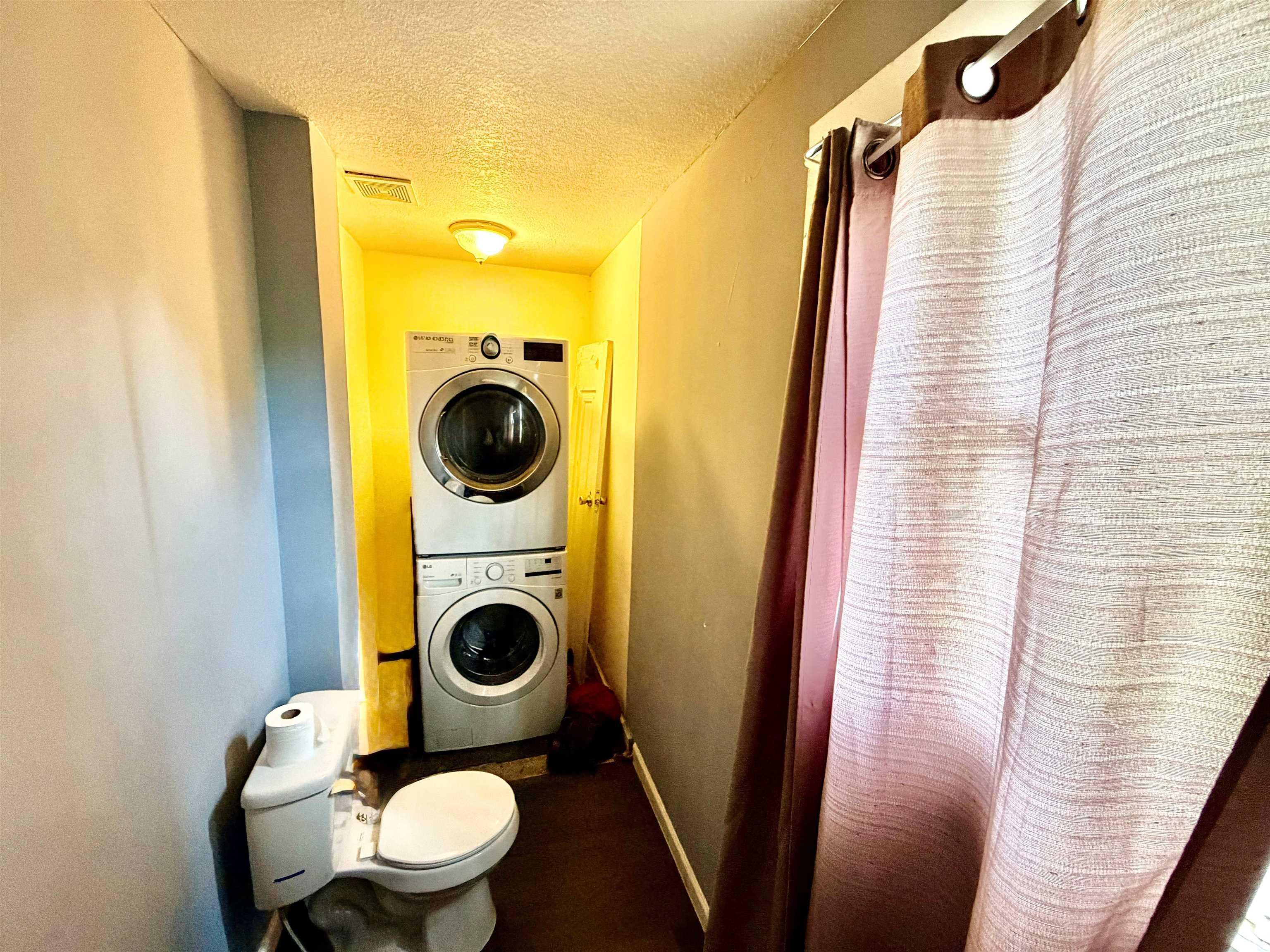 Compact laundry area featuring a stacked washer and dryer unit, integrated into a bathroom space with a white toilet and light-toned walls
