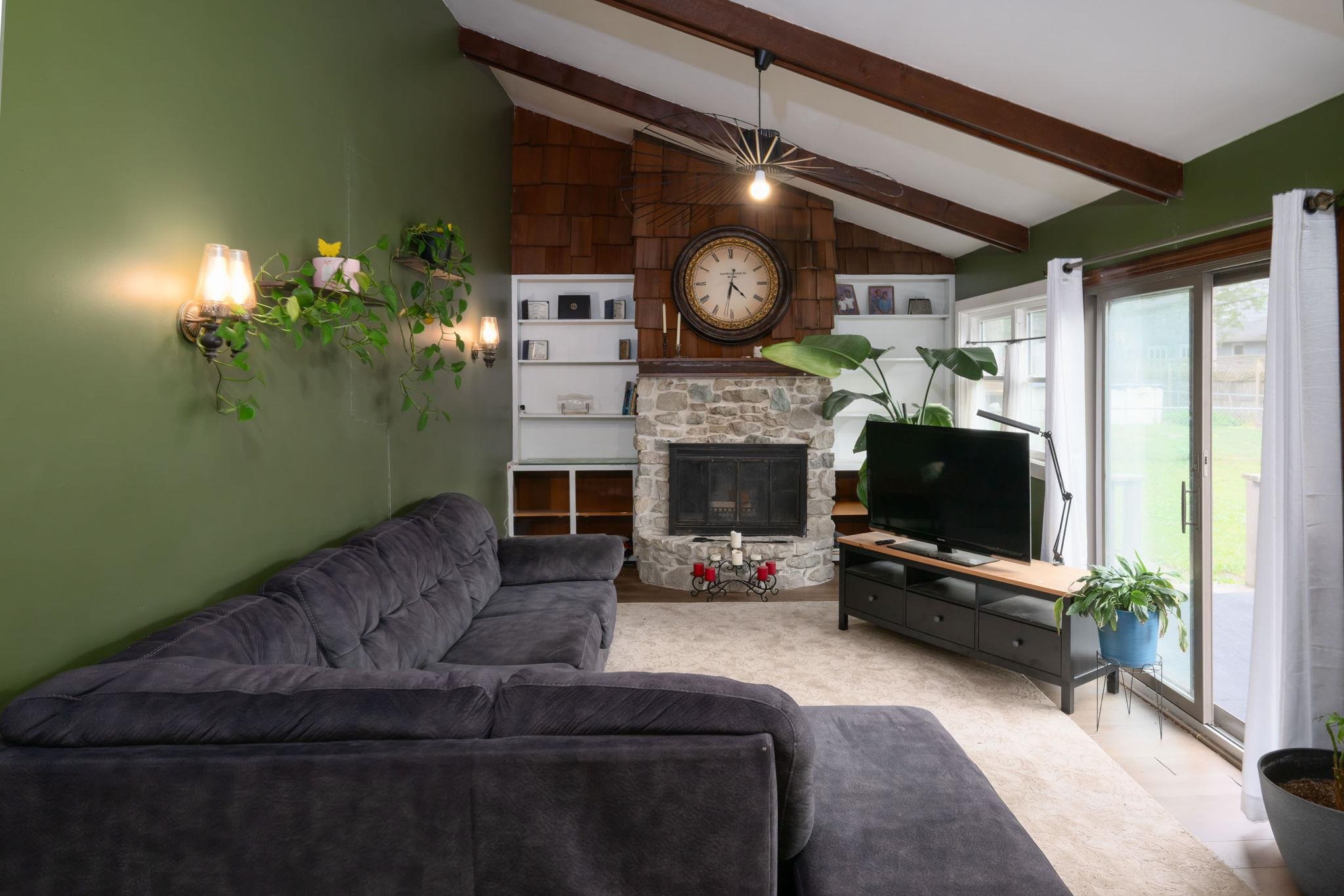 Living area featuring a stone fireplace with a wood-shingled surround, vaulted ceiling with exposed beams, and built-in shelving