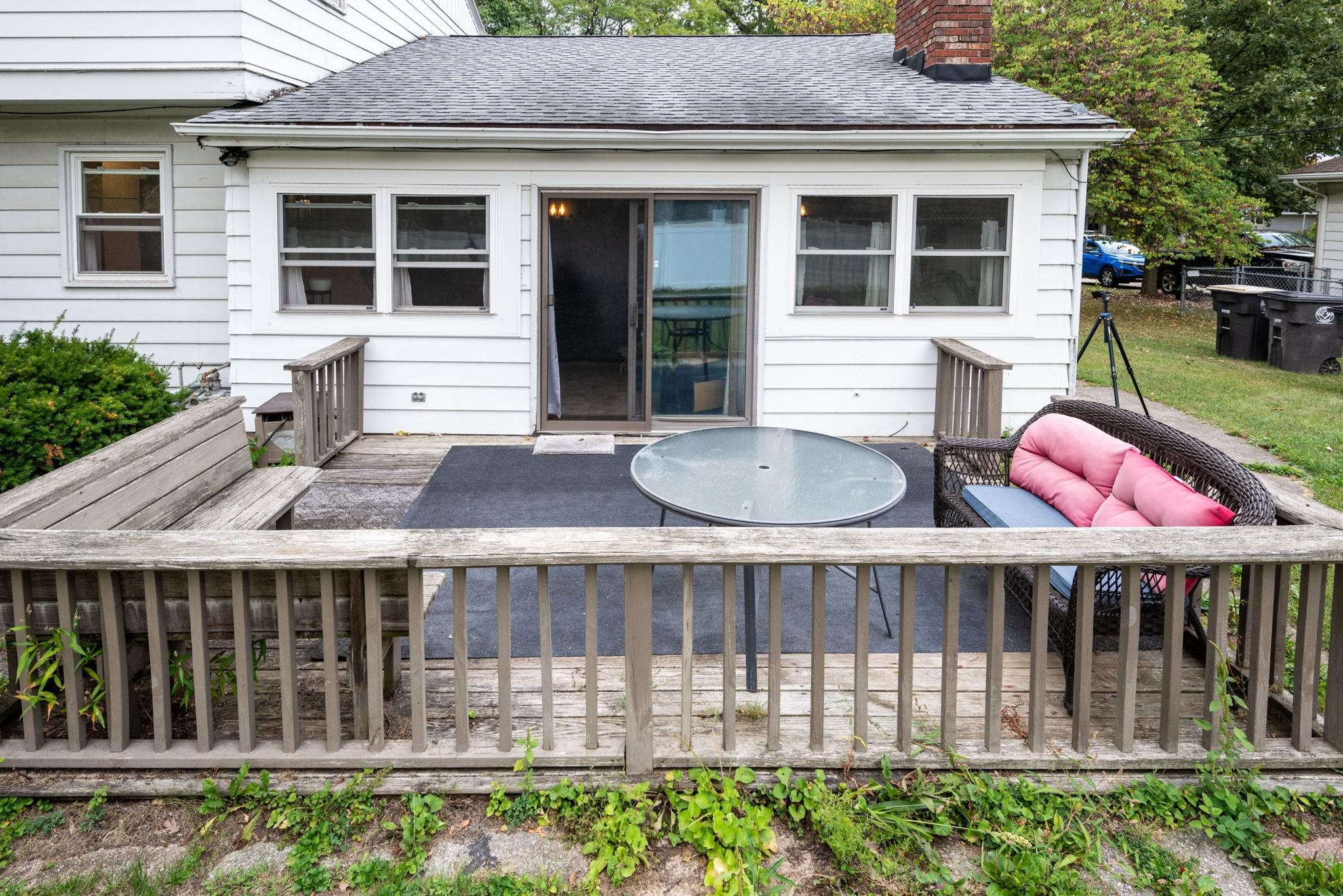 Rear exterior featuring a wood deck with railing, sliding glass door access, white siding, and multiple windows