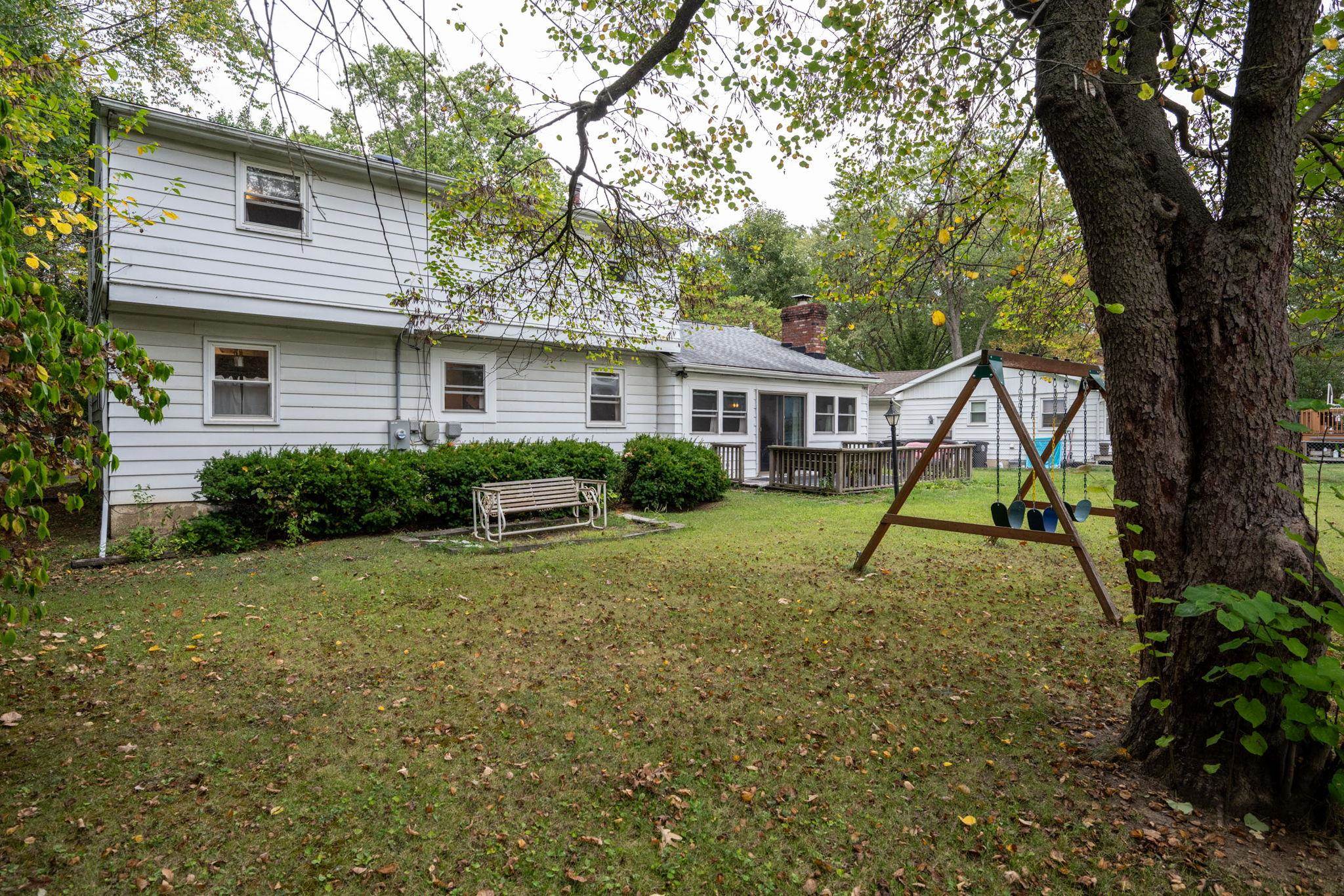 Spacious rear yard with a wooden deck, mature trees, and established shrubbery