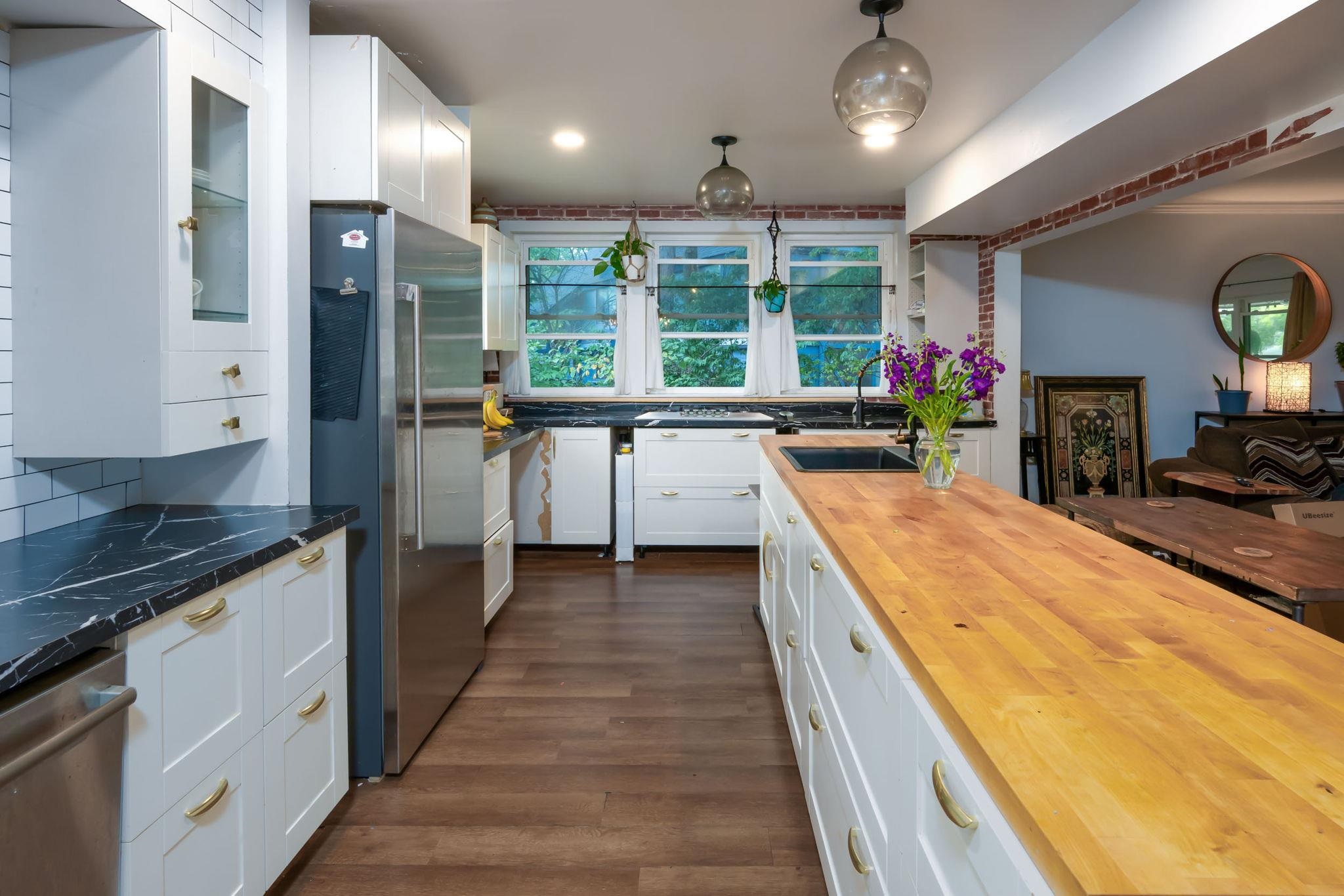 Kitchen featuring a wood-finish island countertop with an integrated sink, white cabinetry with gold-tone hardware, and dark countertops with light veining