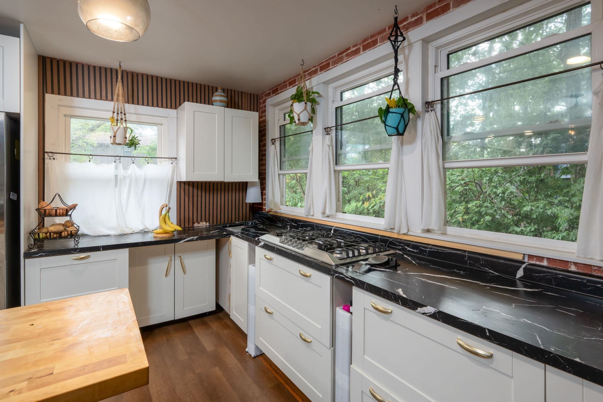 Kitchen featuring white shaker-style cabinetry, black countertops with white veining, a gas range, and wood-finish flooring