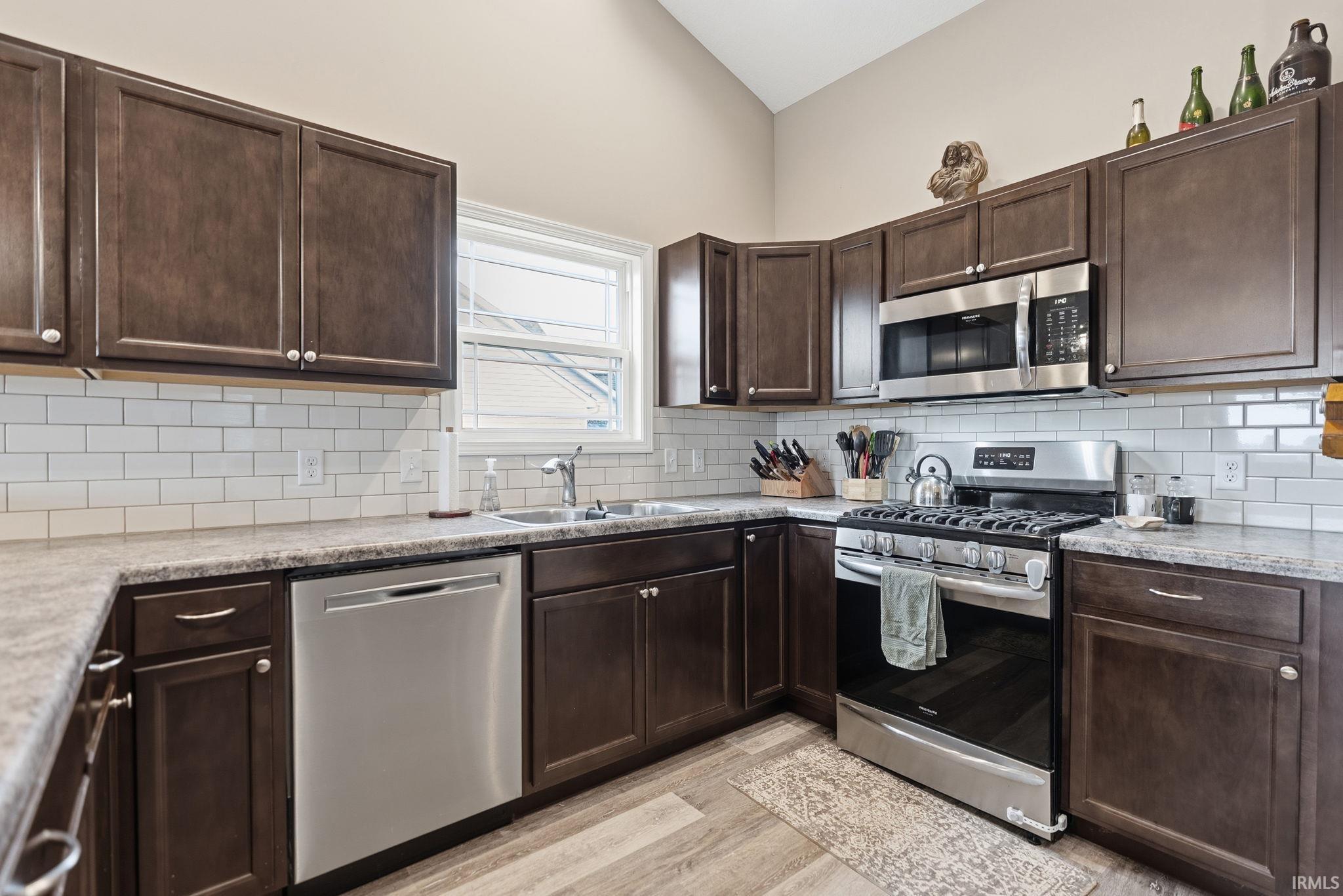 Modern kitchen featuring wood-finish cabinetry, stainless steel appliances, white subway tile backsplash, and light-toned countertops