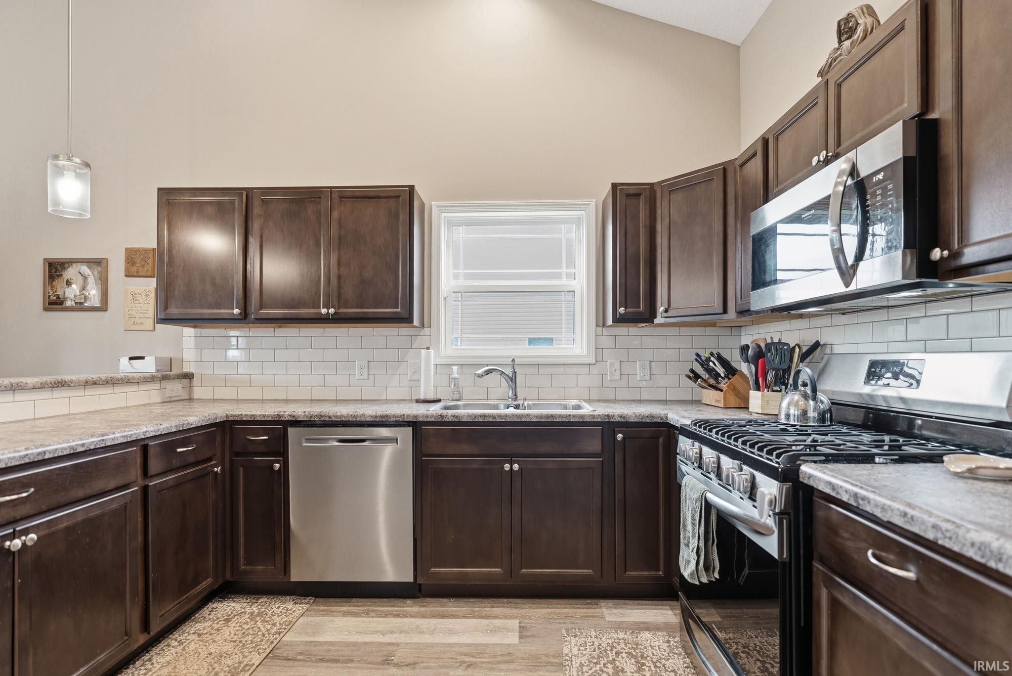 Kitchen featuring dark wood cabinetry, stainless steel appliances, speckled countertops, and a white subway tile backsplash