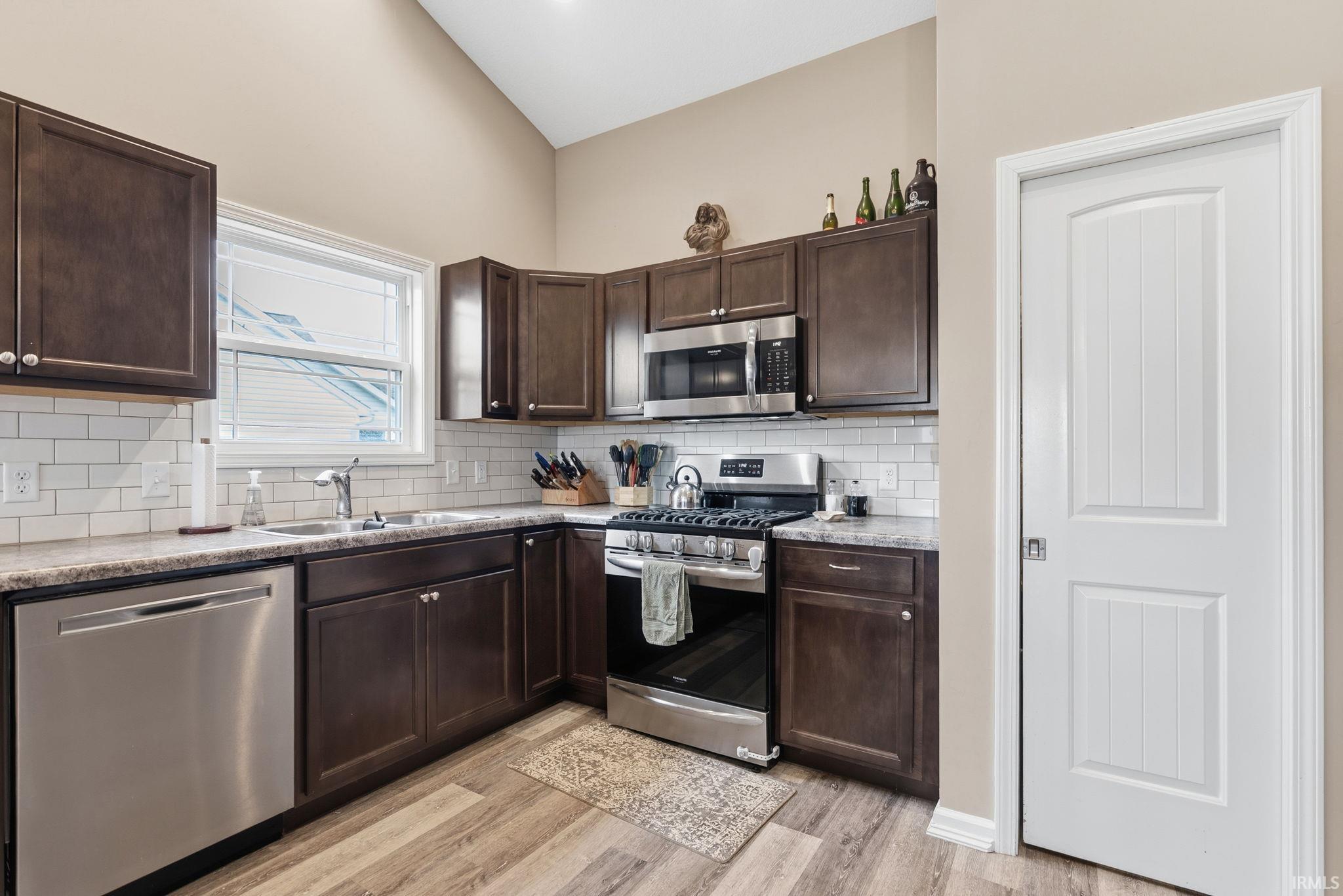 Kitchen featuring dark wood cabinetry, stainless steel appliances, white subway tile backsplash, and wood-finish flooring