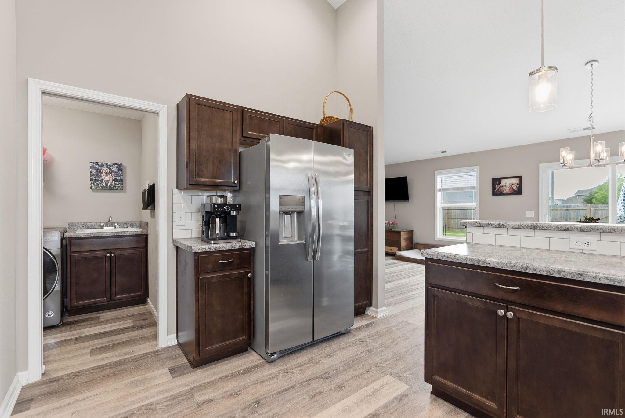 Kitchen featuring wood-finish flooring, dark wood cabinetry, a stainless steel refrigerator, and a white subway tile backsplash