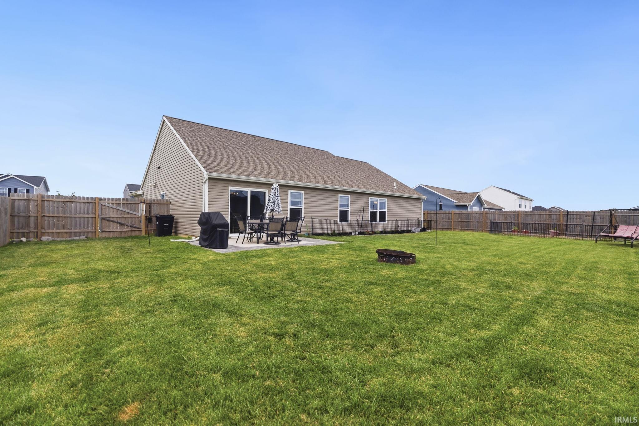 Expansive backyard featuring a manicured lawn, full wood privacy fencing, and a concrete patio with sliding glass door access to the residence