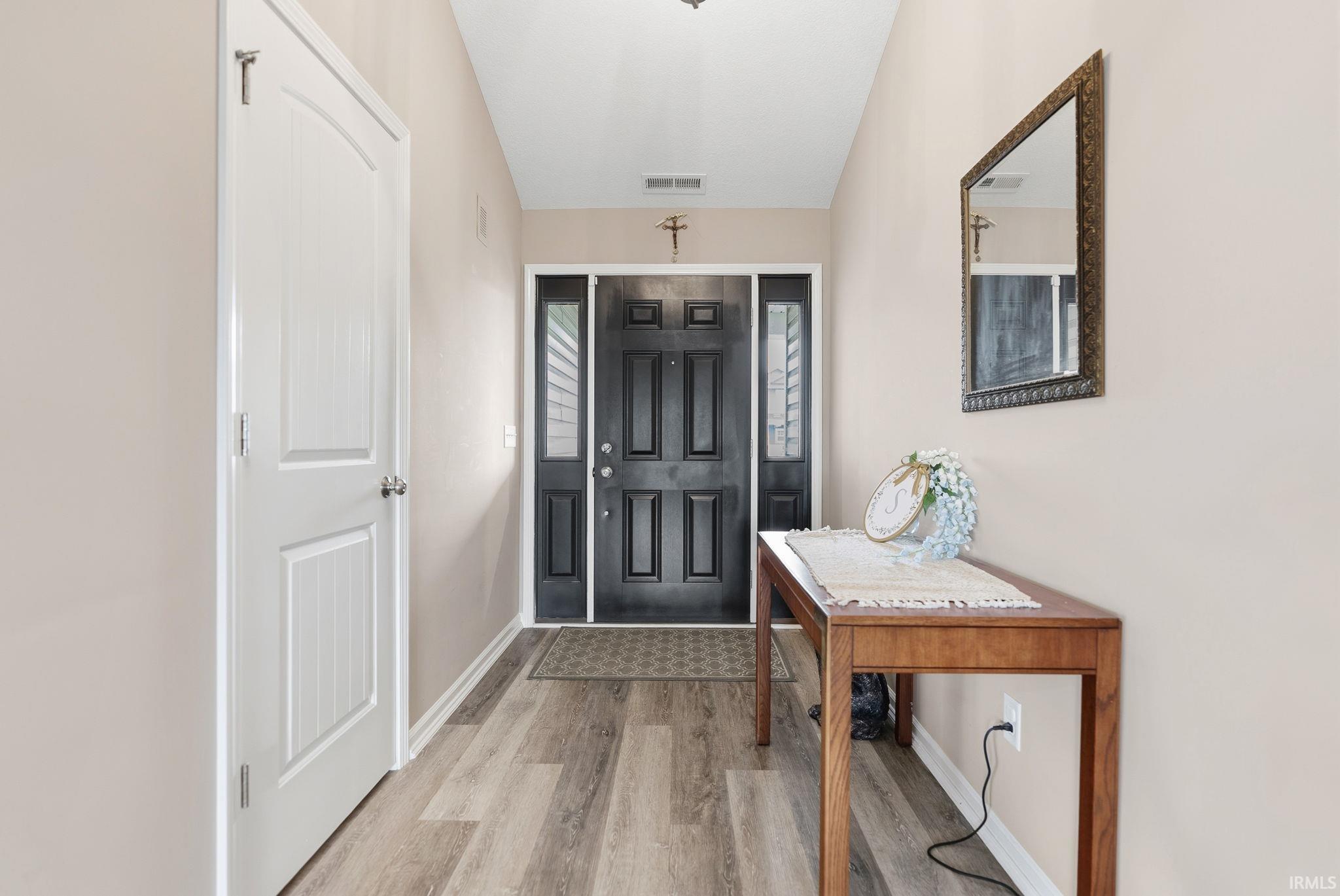 Foyer featuring wood-finish flooring, a black paneled entry door with sidelights, a white interior door, and light neutral wall paint