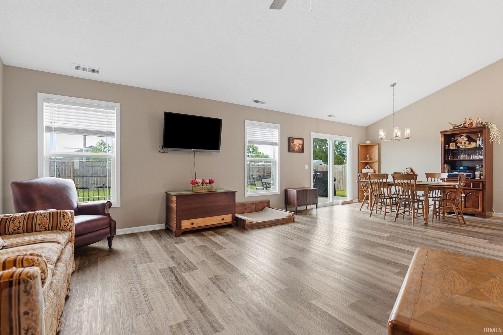 Spacious open-concept living area featuring wood-finish flooring, vaulted ceilings, and neutral wall tones