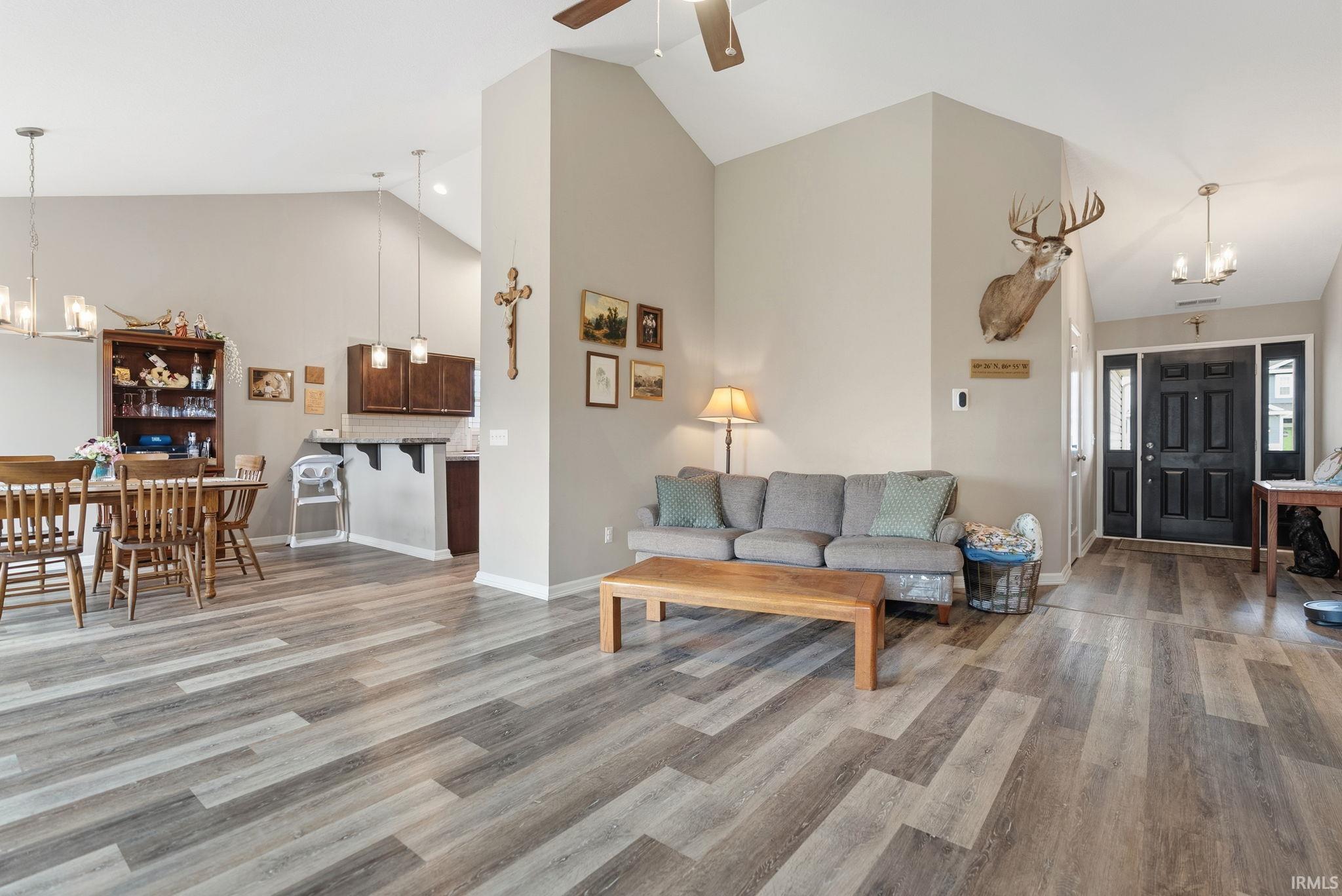 Open-concept interior featuring light gray walls, vaulted ceilings, wood-finish flooring, a black front entry door with sidelights, and recessed lighting
