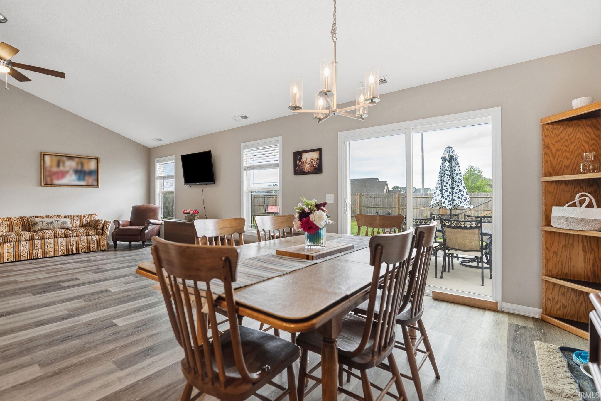 Open concept living and dining area featuring wood-finish flooring, vaulted ceilings, and a contemporary chandelier