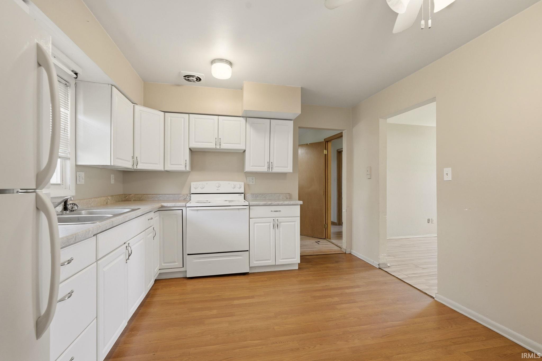 Kitchen featuring wood-finish flooring, white cabinetry, a double basin sink, and a white appliance suite