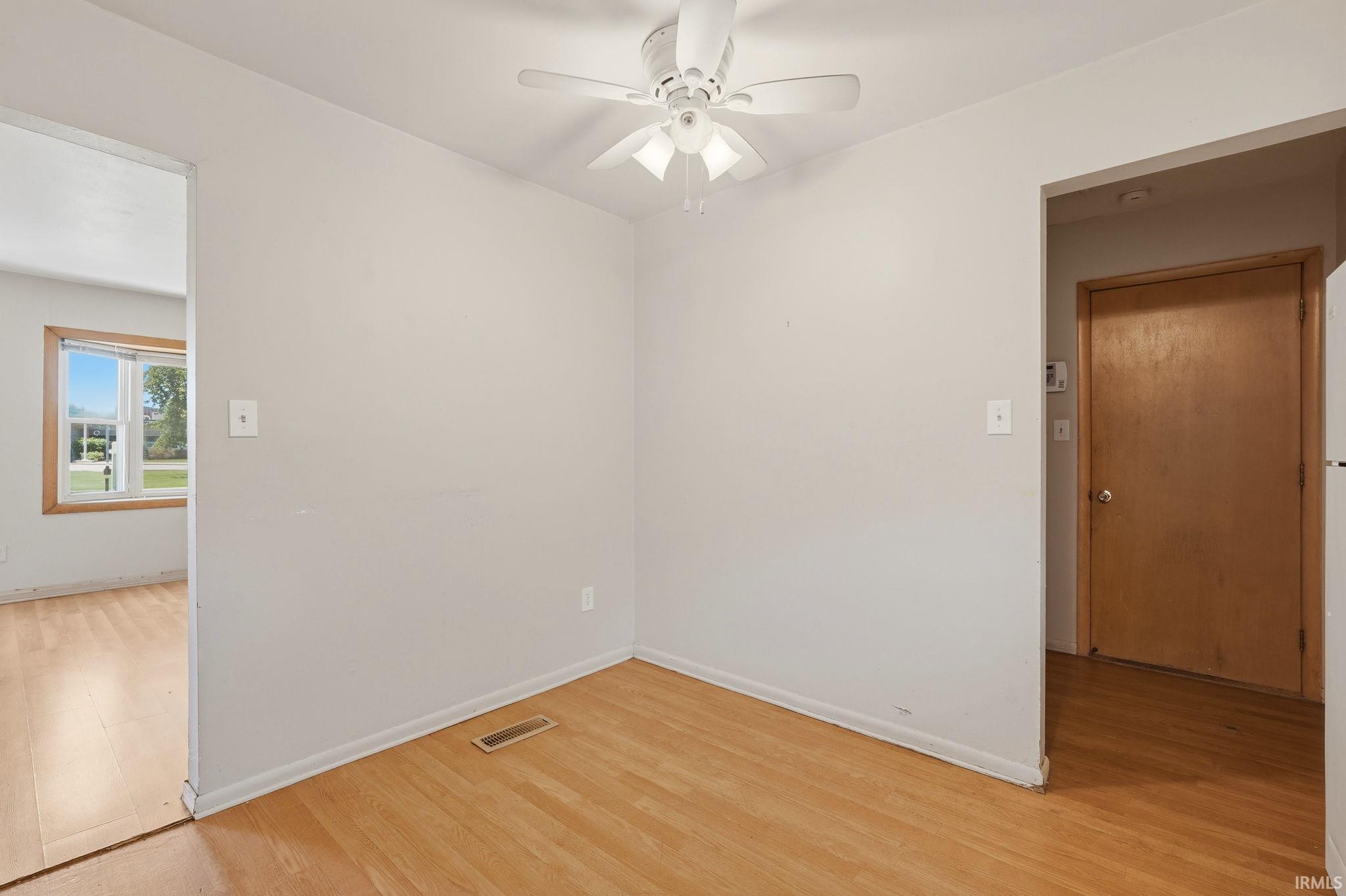 Light-filled interior space featuring wood-finish flooring, a white ceiling fan with integrated lighting, and neutral wall tones