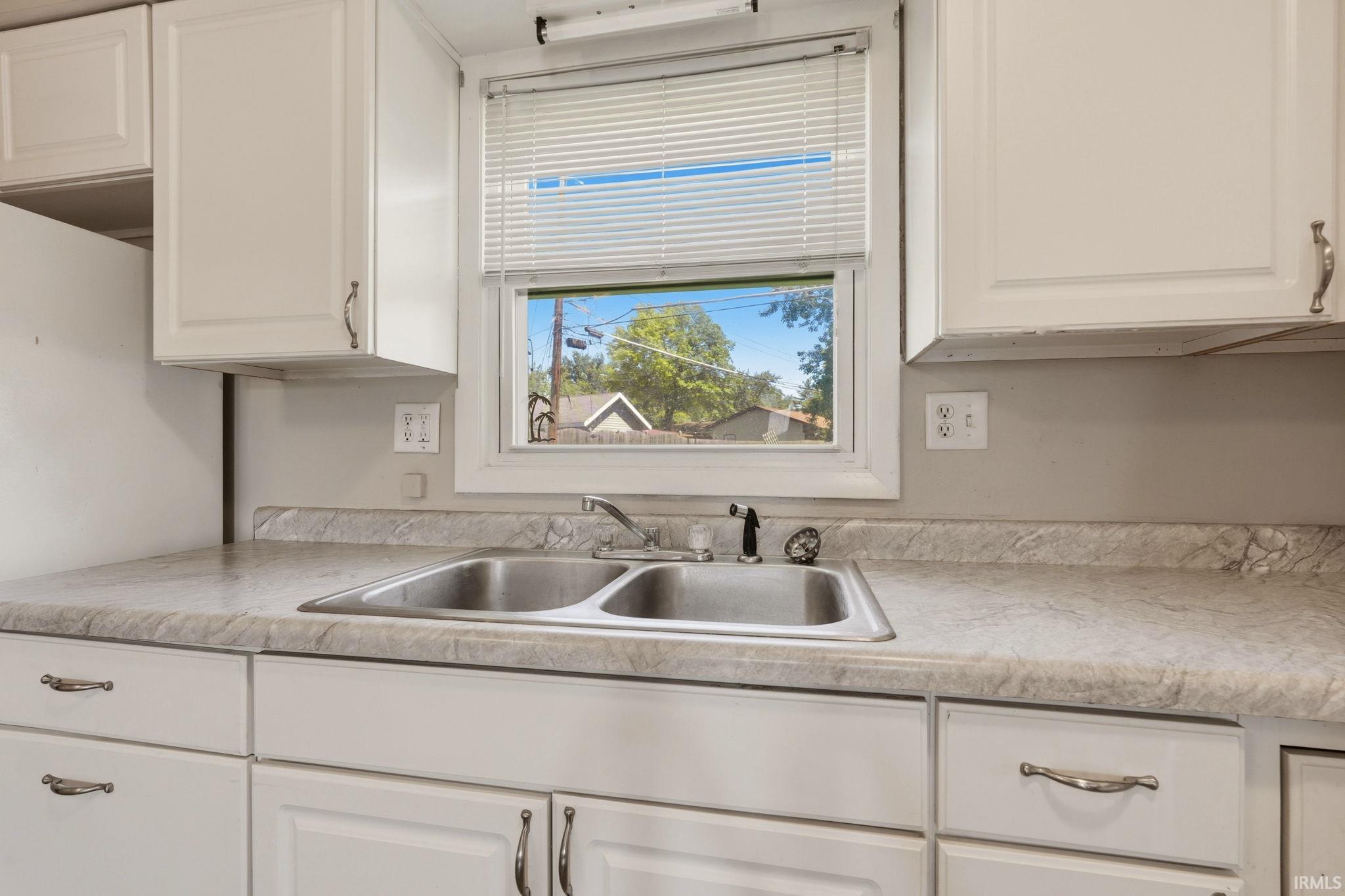 Kitchen featuring white cabinetry with brushed nickel hardware, a double basin stainless steel sink with a single-handle faucet, and light-toned countertops